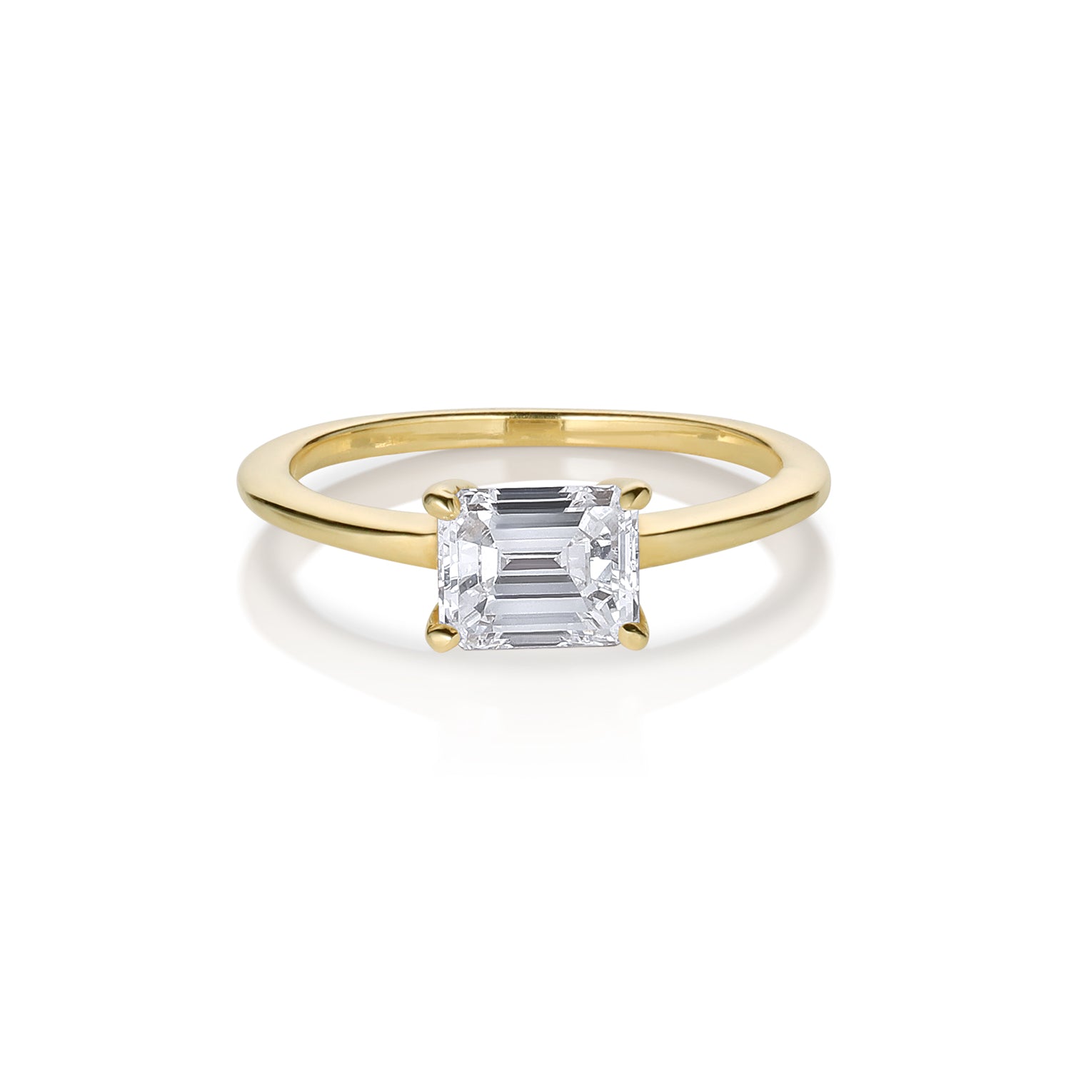 A 14k gold ring featuring a sideways set emerald cut white diamond in a solitaire setting with a narrow band.