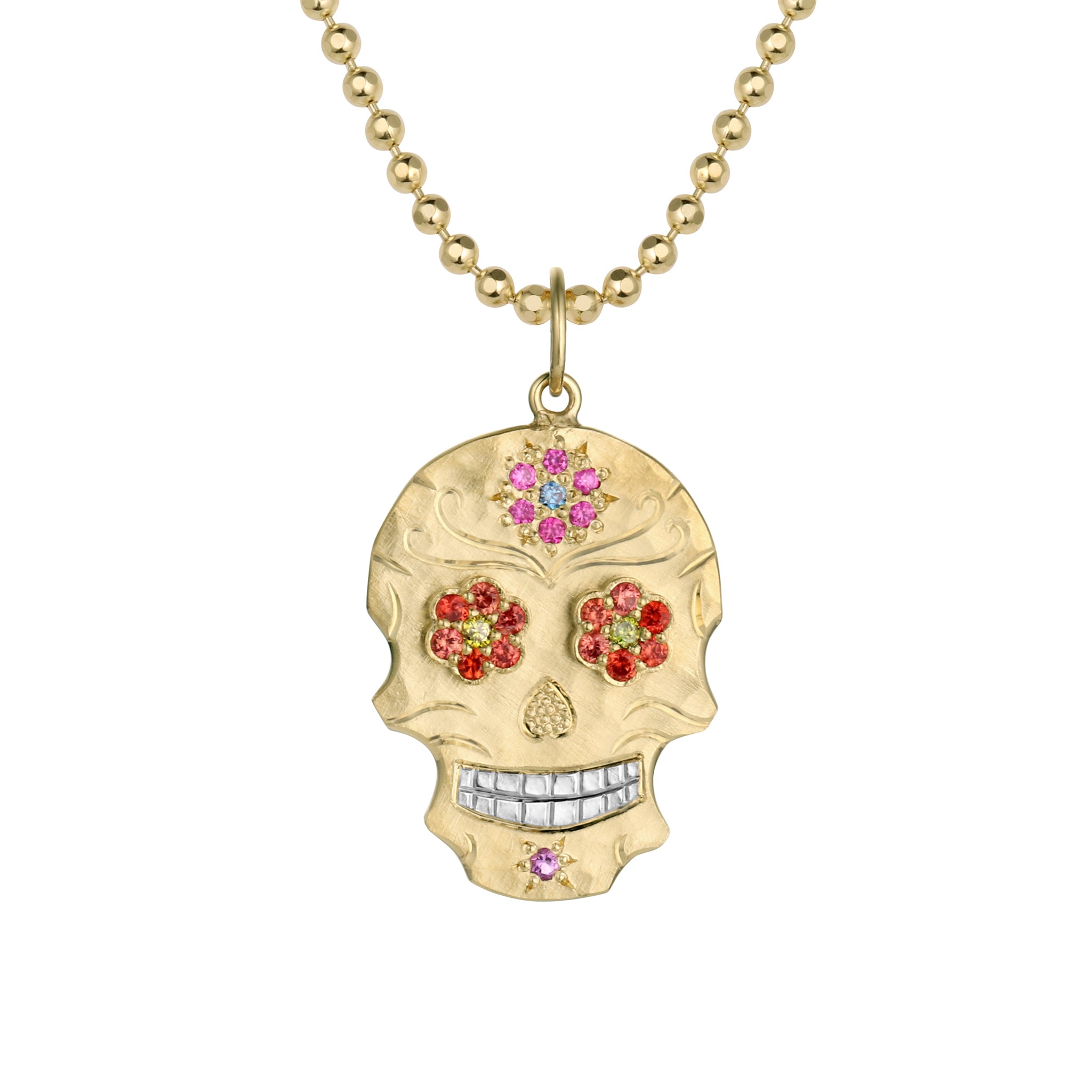 Small 14k gold skull shaped pendant necklace with orange and yellow bezel set gemstone floral eyes, pink and blue bead set pink and blue flower on forehead, hand engraved details and shiny rhodium plated teeth hanging on 14k gold ball chain shown on a white background.