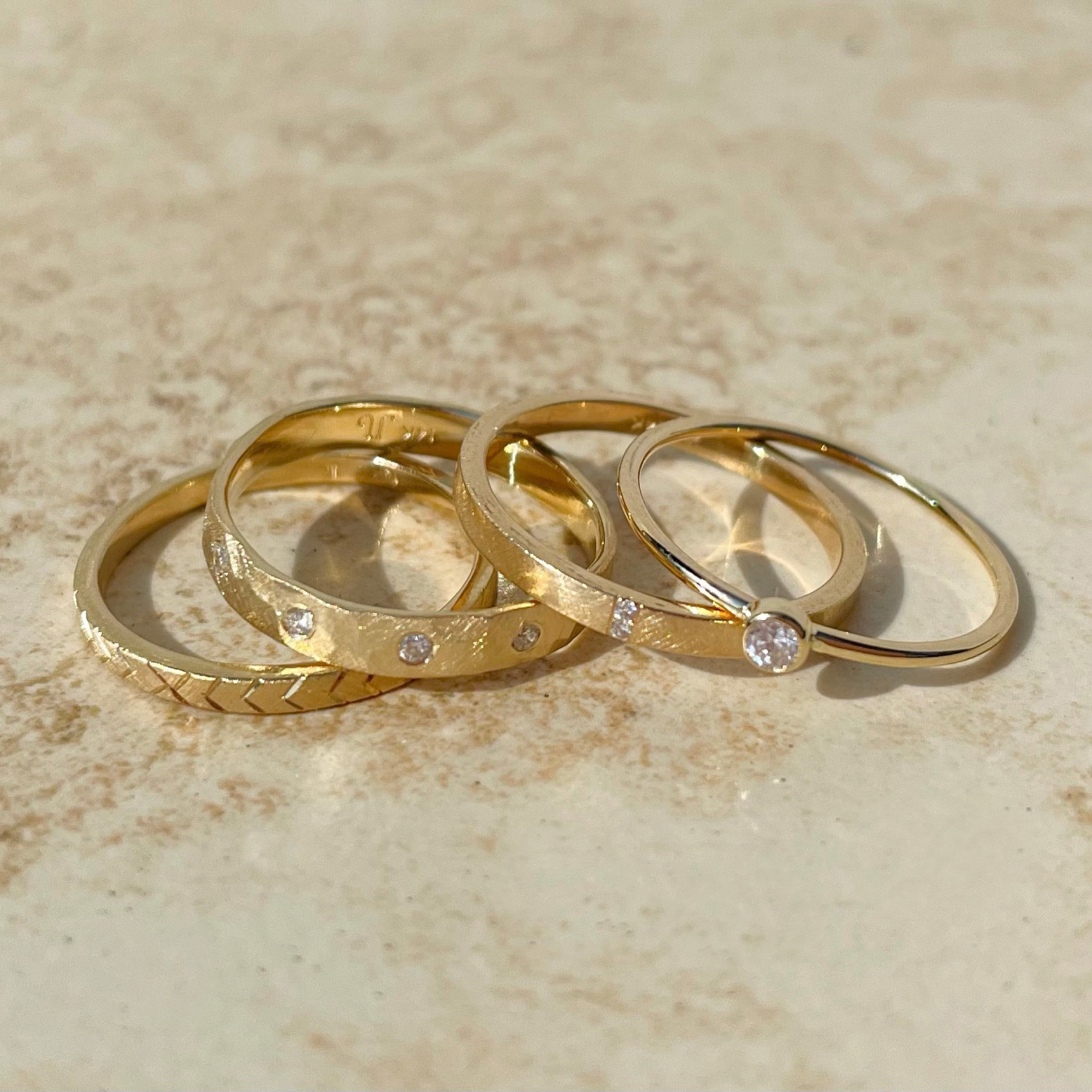 14k yellow gold stackable rings including the gela ring with geometric etching on it with the gelb ring and the raya ring and the gelb ring by julez bryant in lifestyle shot on natural surface background