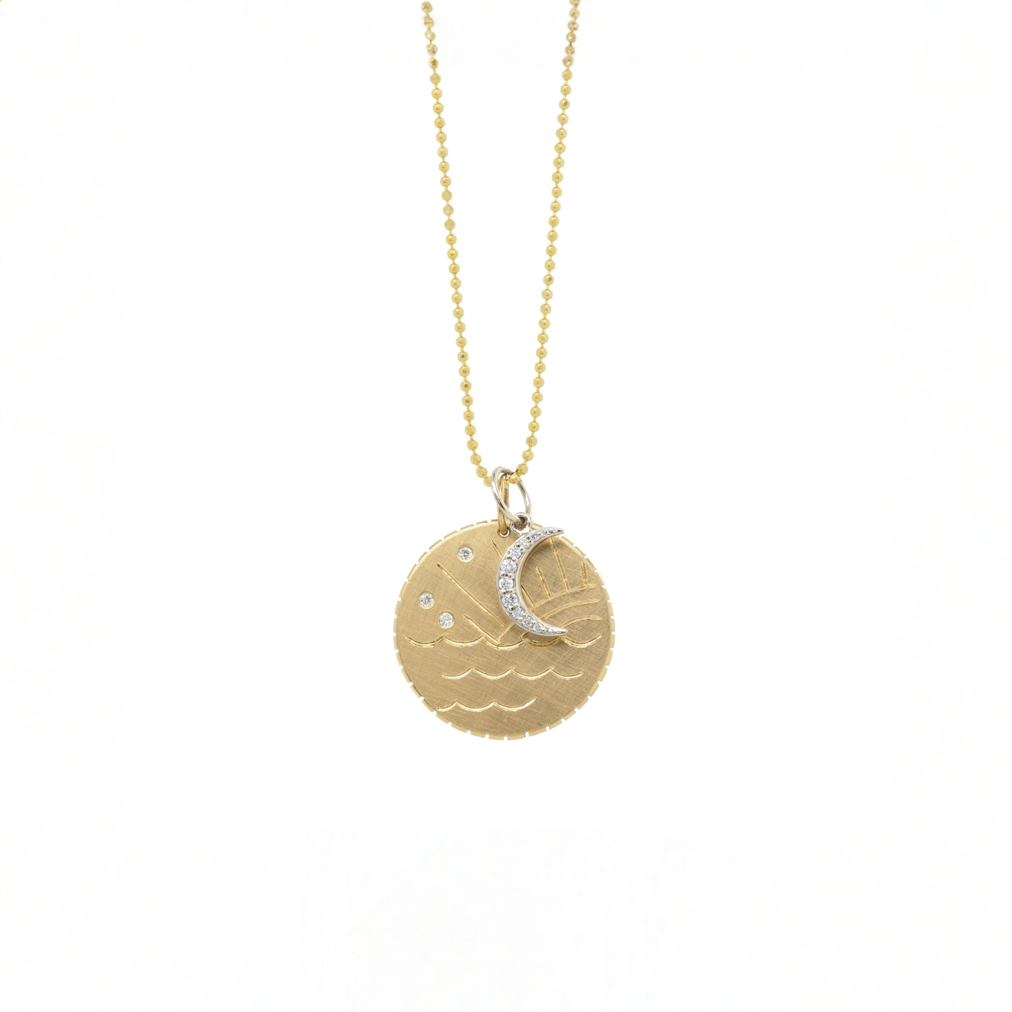 14k yellow gold round diamond disk pendant necklace featuring hand engraved ocean waves and sun ray design scattered white diamonds in the sky and notched detail around edge shown layered with white gold diamond pave charm hanging from round ball chain on white background