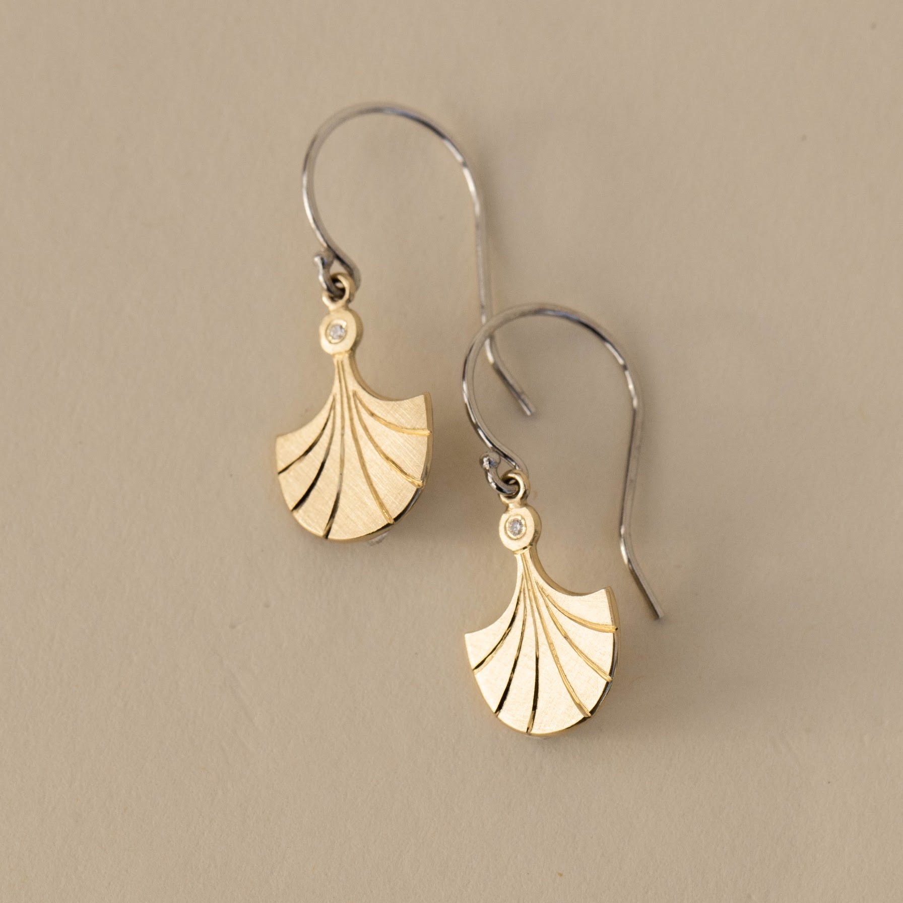 Two tone white and yellow gold fan shaped drop earrings with small diamond accent on french wire lifestyle shot on neutral background