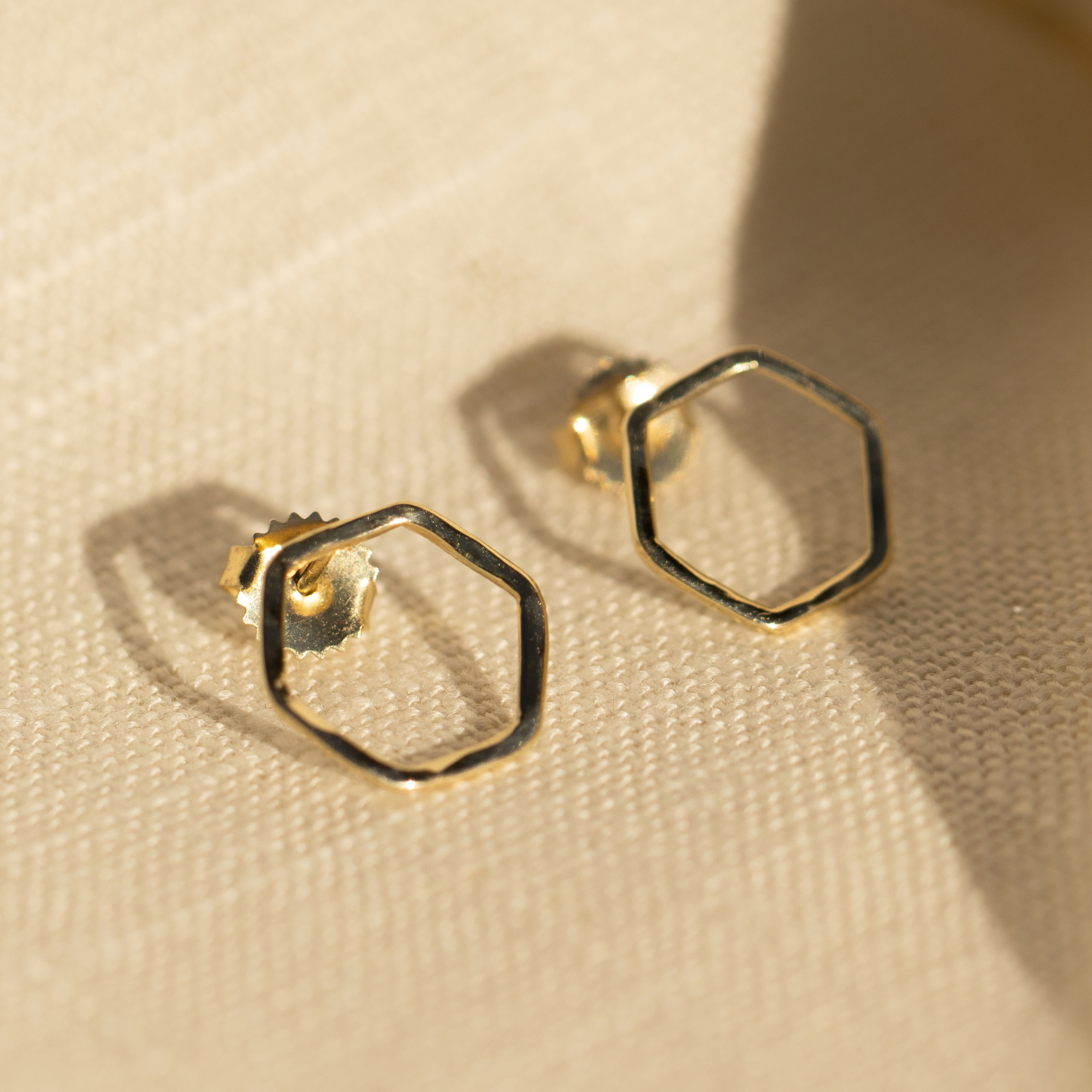 14k yellow gold open hexagon stud earrings on tan background