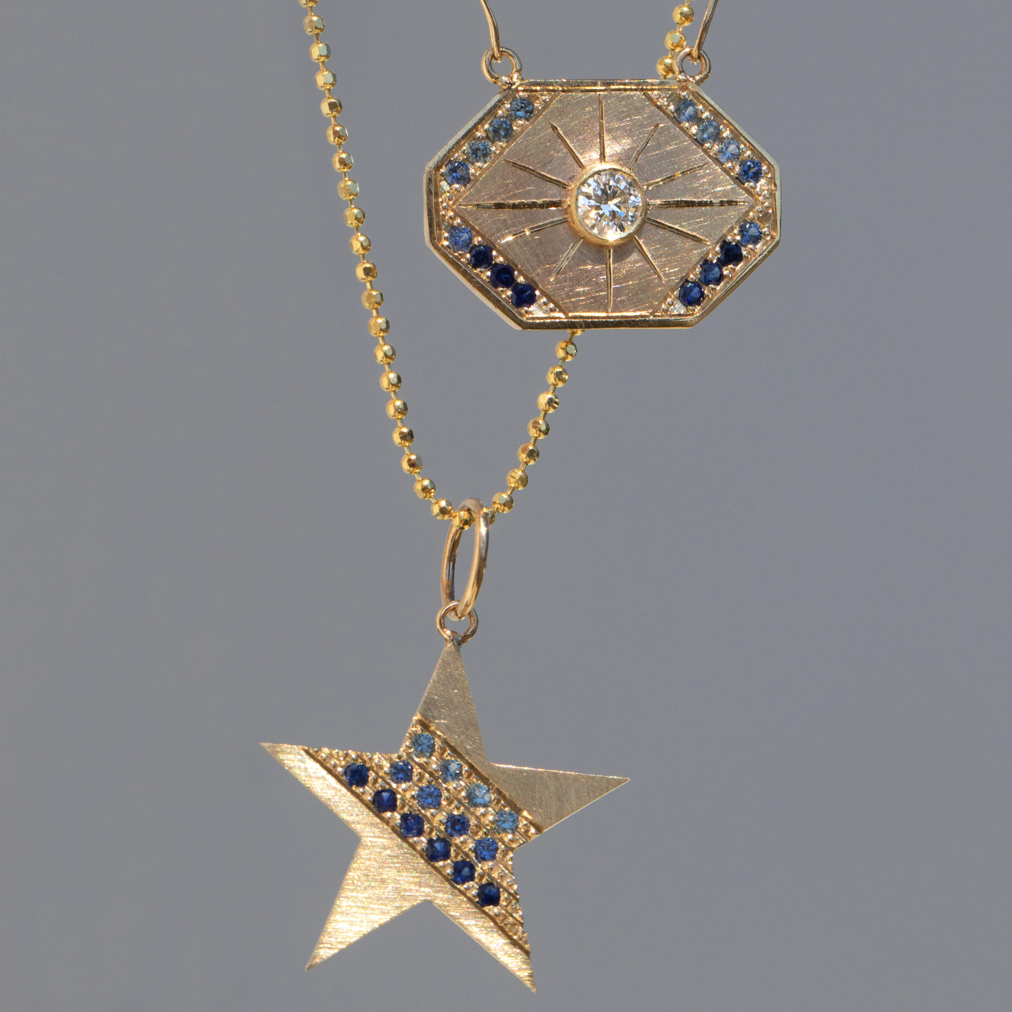 14k yellow gold star-shaped pendant with paved-set colored sapphires on a diamond cut ball chain paired with the dusk necklace on a blue background