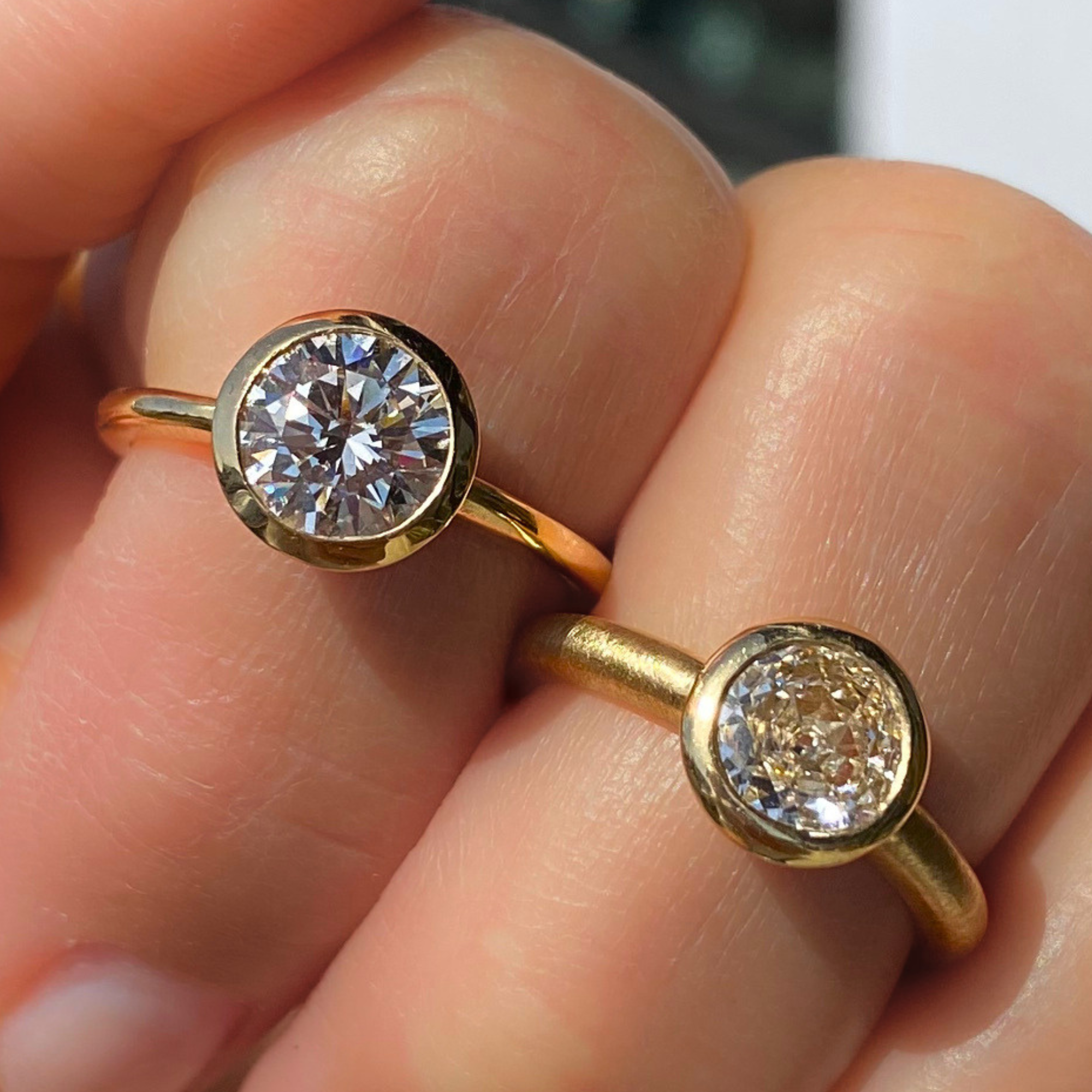 Image of two lab grown bezel solitaire round brilliant brilliant 14k yellow gold engagement rings candid on models hand
