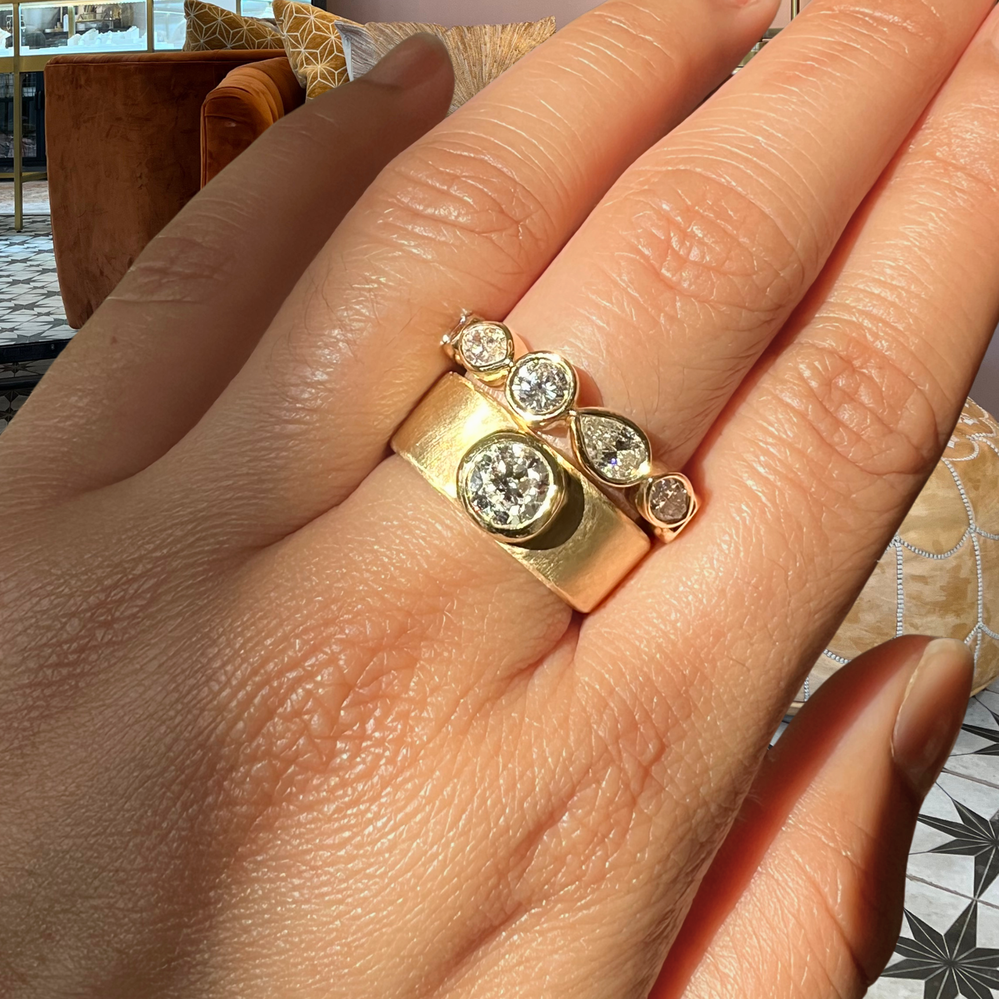 Image of a lab grown round brilliant bezel solitaire thick cigar band 14k yellow gold engagement ring candid blurred background.