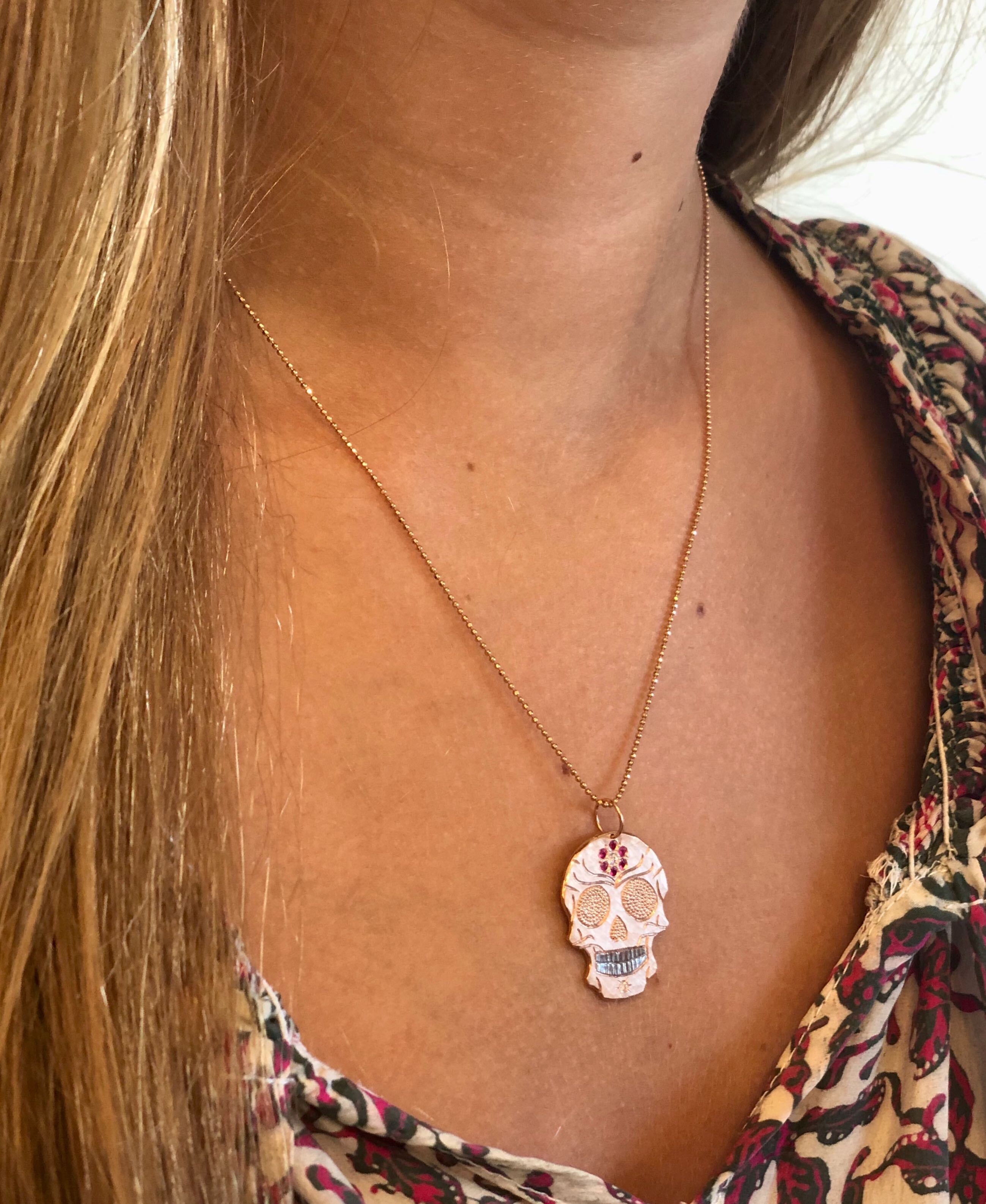 14k yellow gold and pink sapphire Skull pendant necklace on a person wearing a floral top
