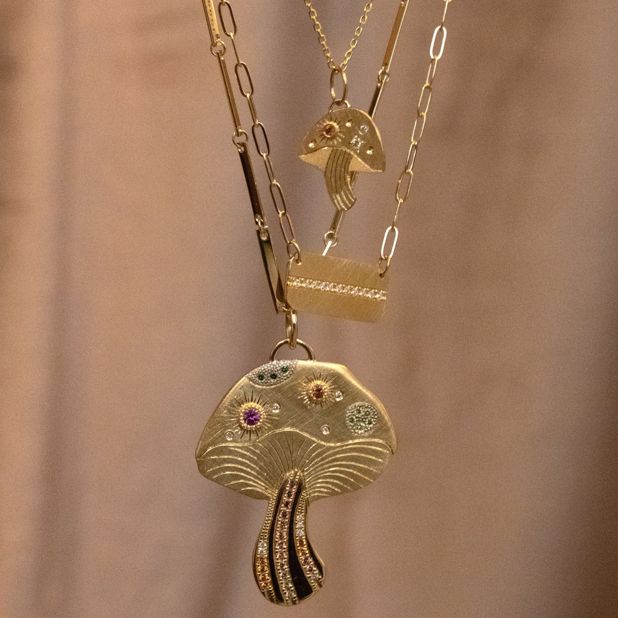 14k yellow gold extra large mushroom pendant with colored gemstones and white diamonds with hand etched details stacked with luma pendant and maly necklace with tan background