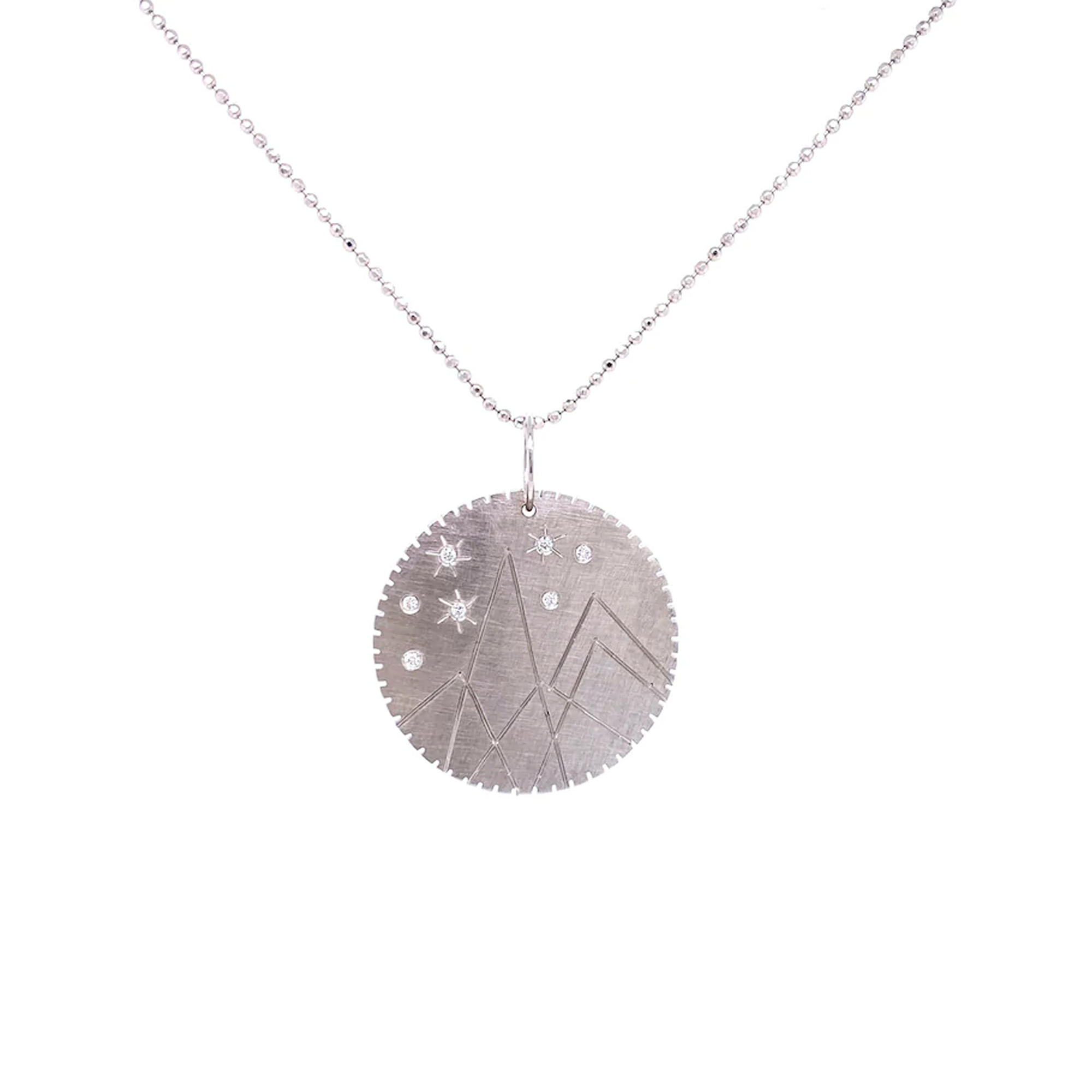 14k white gold round pendant with hand etched mountains and white diamond starbursts on a white background
