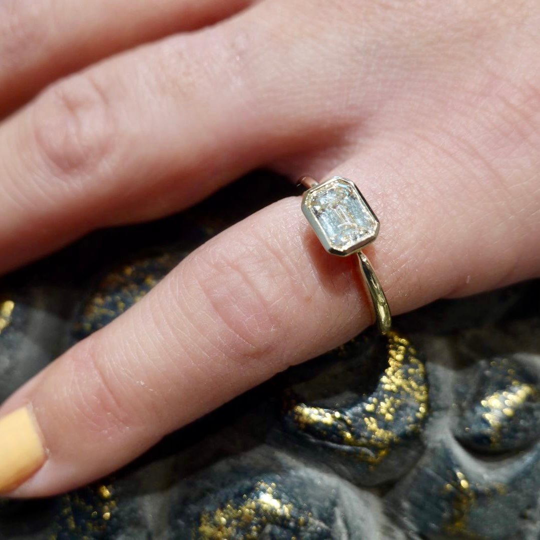 Asscher cut gold solitaire ring with a diamond on a person's finger against a textured background