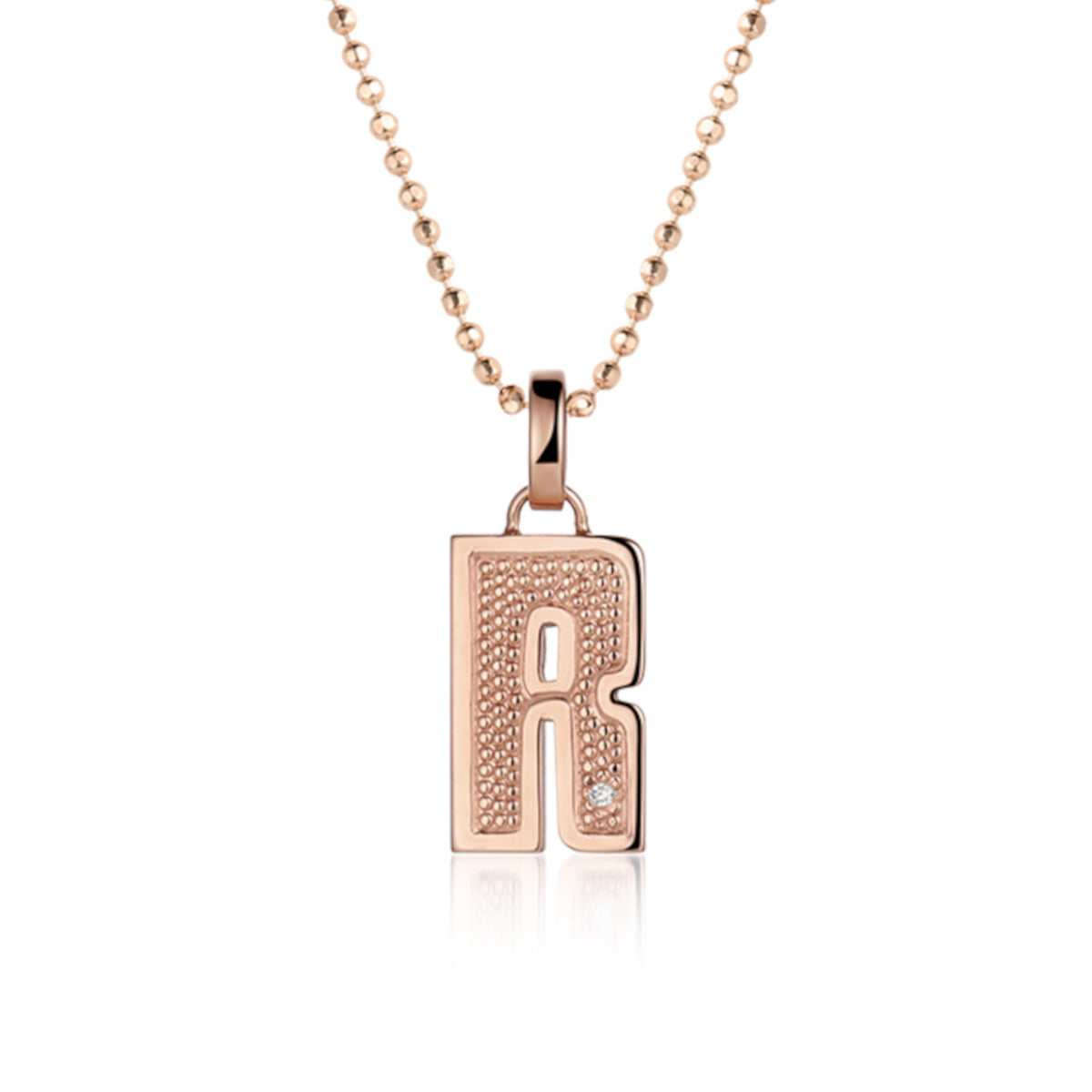 14k rose Gold pendant shaped like the letter R  features single white diamond accent with  textured surface. Pendant on diamond ball chain, shown on white background.