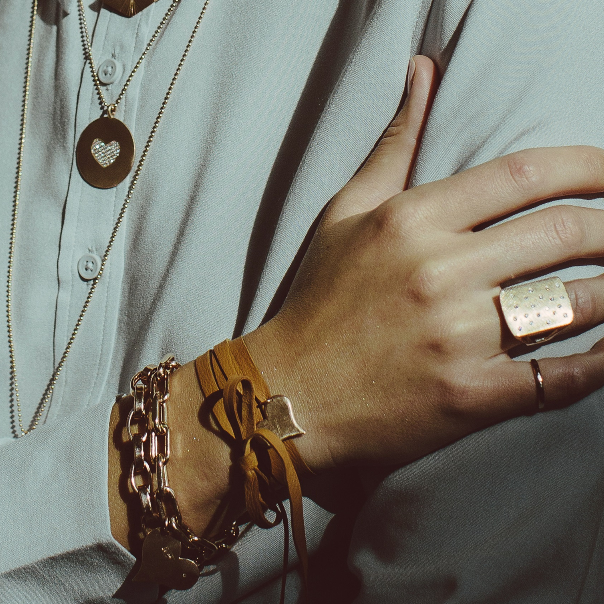 Close-up of a hand wearing multiple gold bracelets and rings on a light gray background