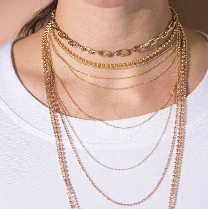 Close-up of a person wearing multiple gold necklaces with different weights and lengths 14k yellow and rose gold on a plain background