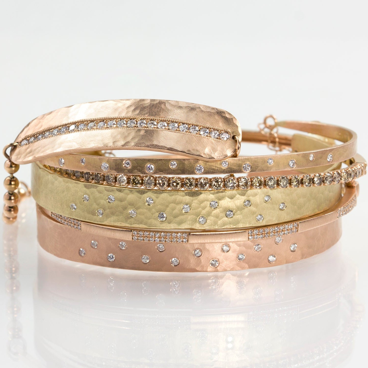 Set of gold bracelets with different designs and scattered white diamonds on a white background