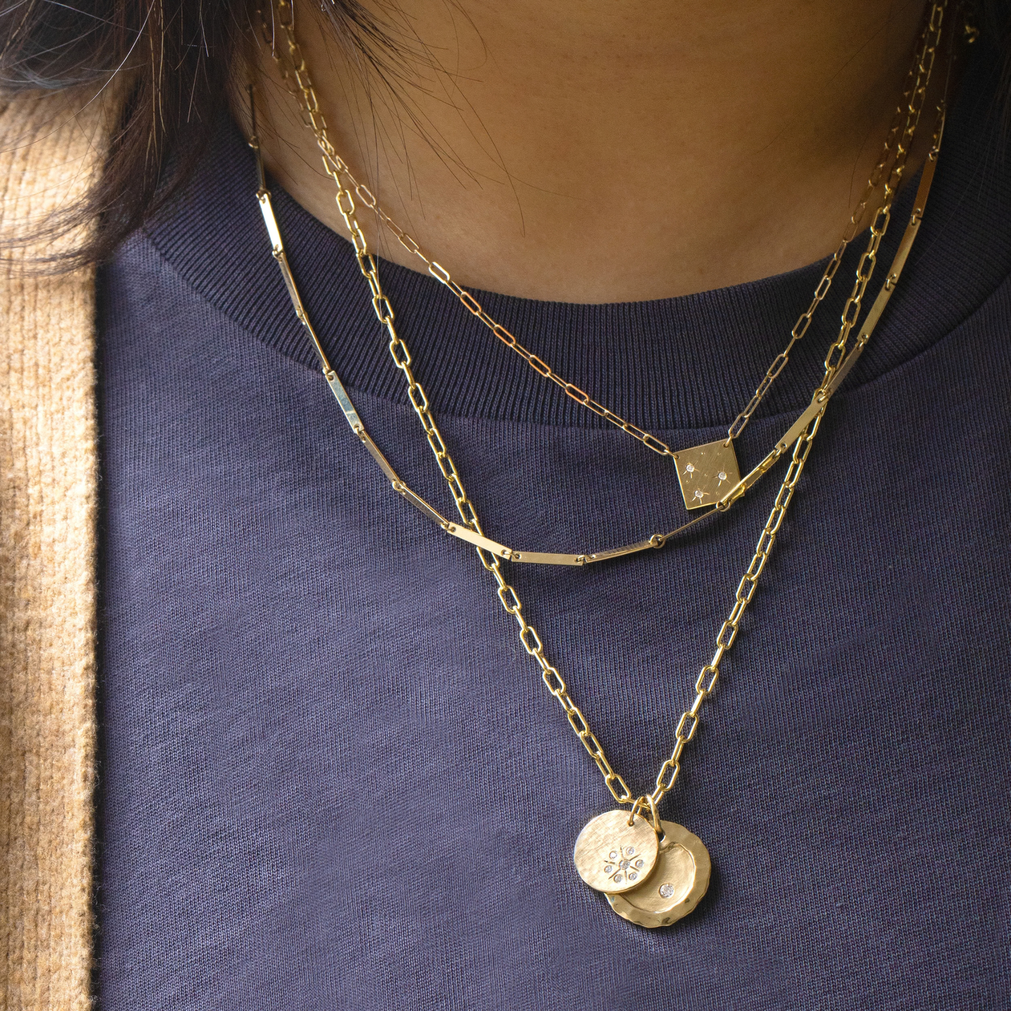 14k yellow gold morz necklace featuring hand etched starbursts and white diamonds stacked with the doey chain and the rl32 chain with the skye and salk round pendants by julez bryant on model in lifestyle shot
