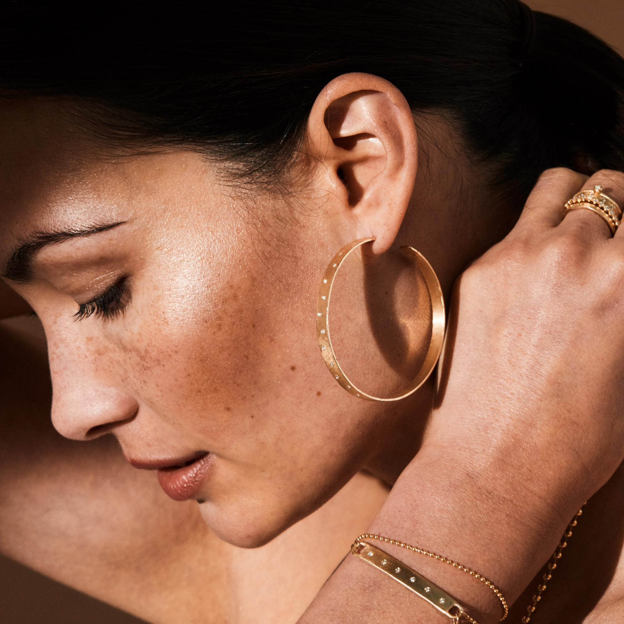 A pair of 14k gold large hoop earrings with a hammered, satin finish and scattered diamonds on model in lifestyle shot