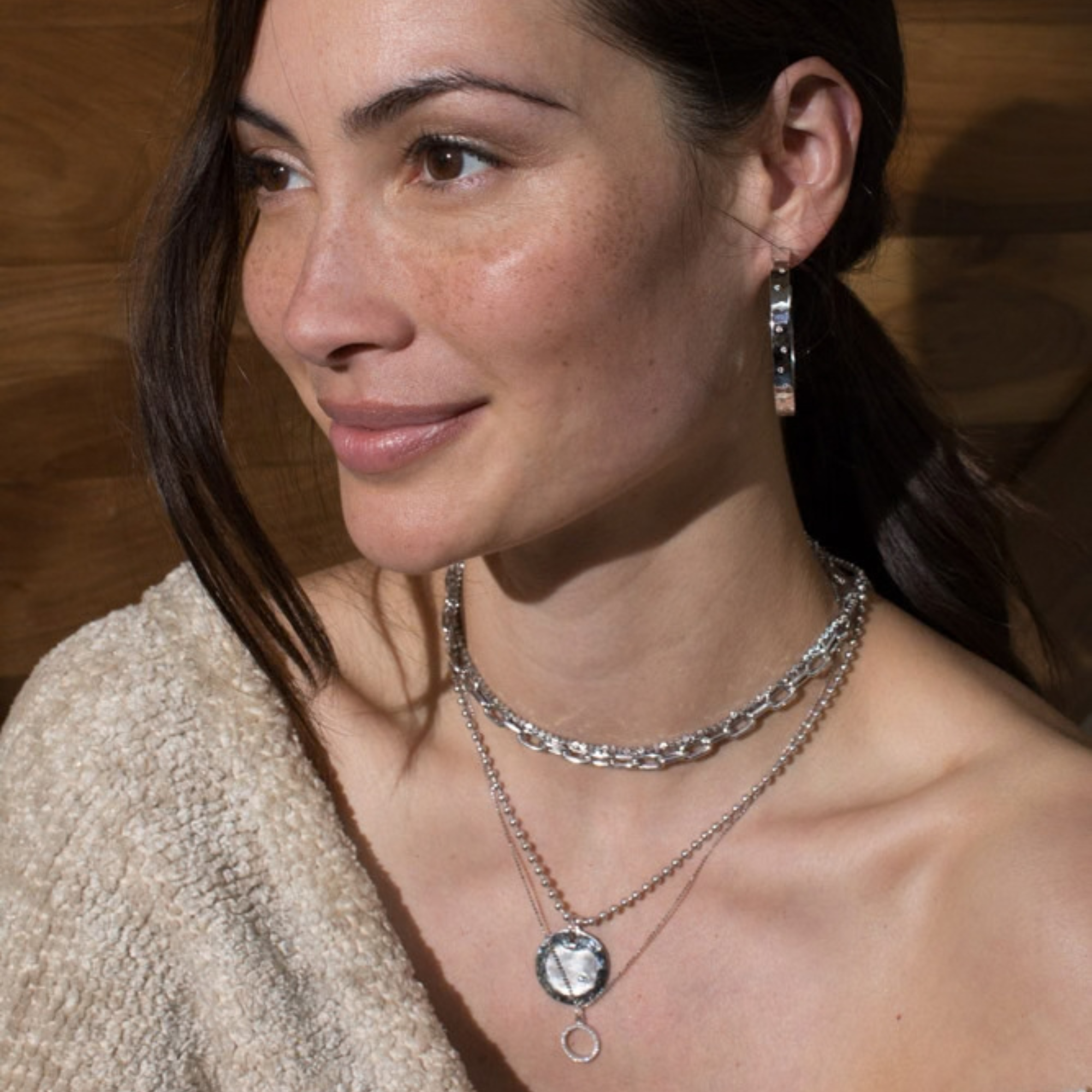14k white gold round pendant with shiny and satin finished and an offset white diamond stacked with the mica chain and moca chain in white gold paired with the opar white gold shiny hammered hoop earrings with white diamonds on model in lifestyle shot