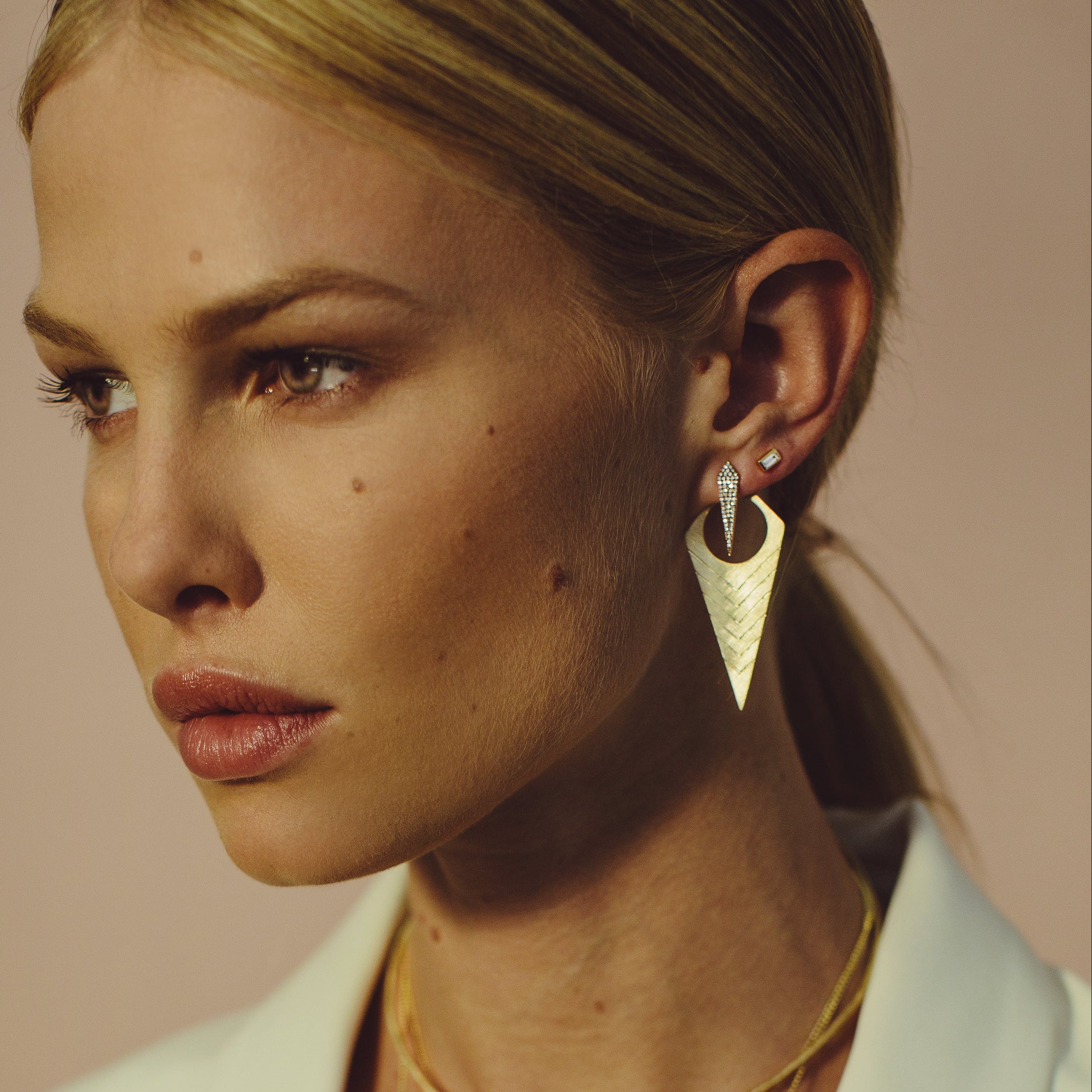 Woman wearing gold earrings with diamonds art deco style geometric large jacket earring paired with minimal baguette stud  with a plain background