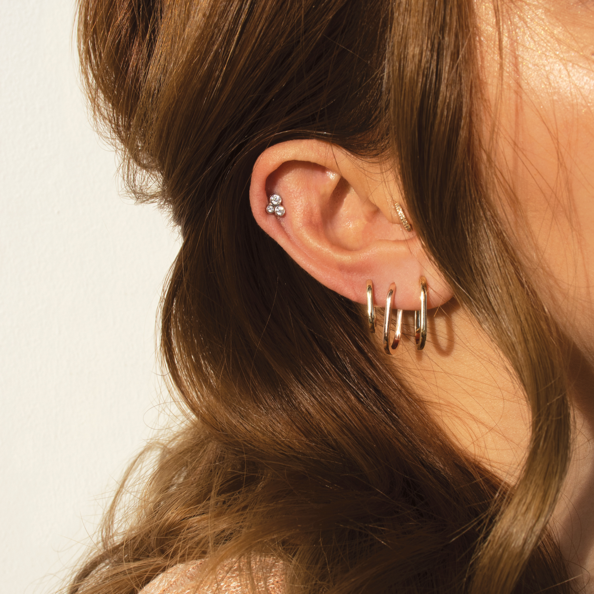 14k yellow gold triple diamond bezel stud earrings paired with elsi hoops on model in lifestyle shot