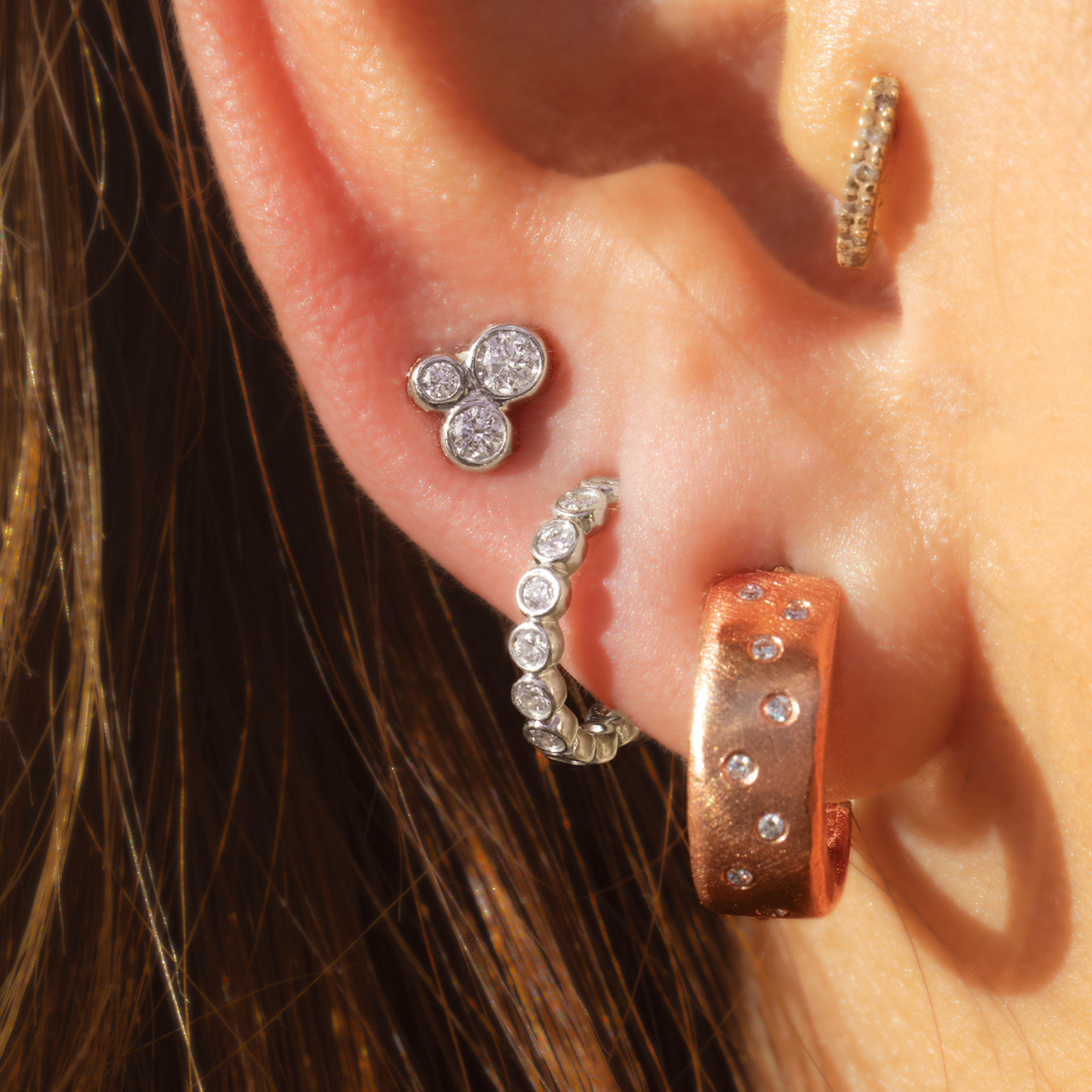 Close up of ear wearing stacked earrings including diamond huggie hoops and studs