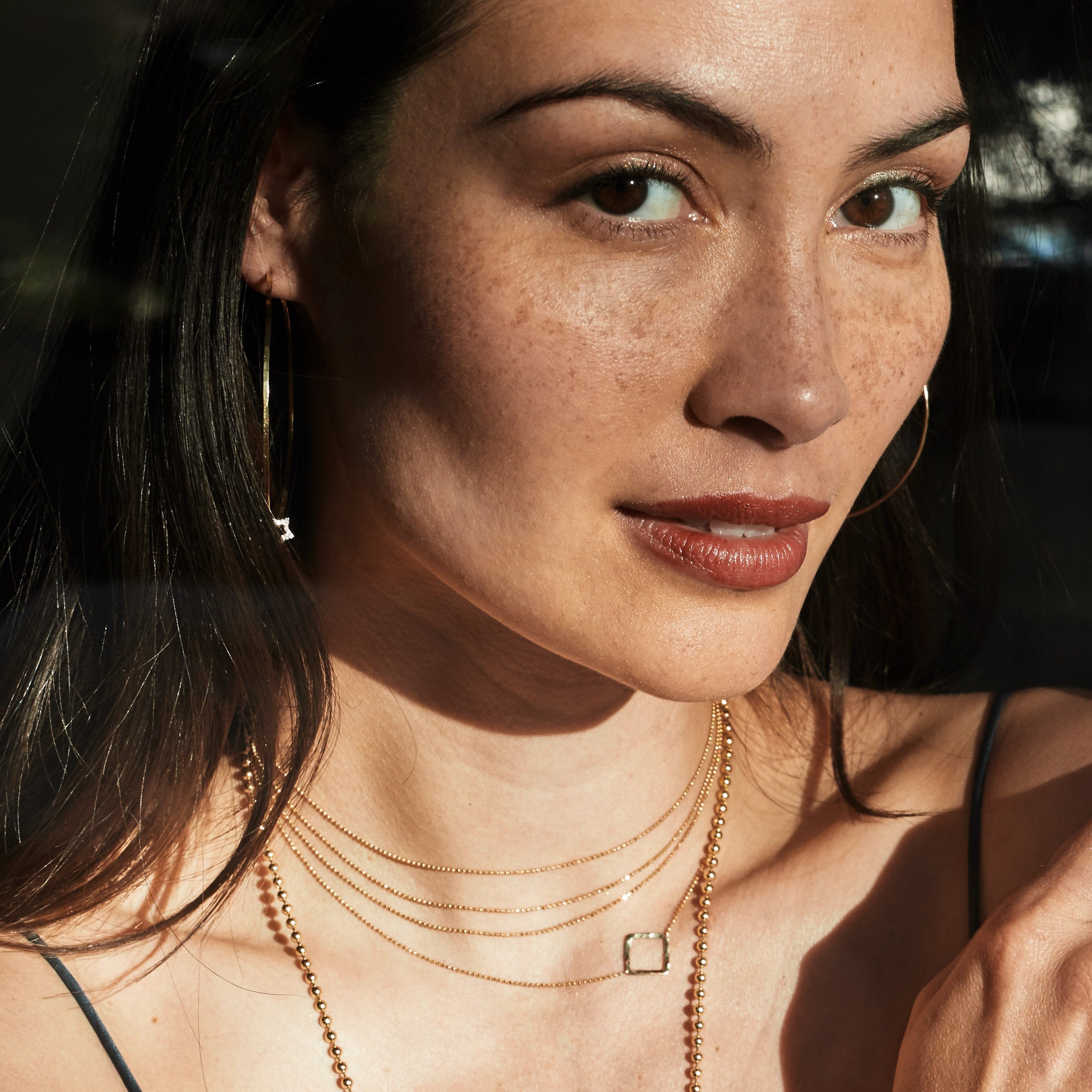 Woman wearing 14k gold jewelry close up of layered diamond ball chain chokers with integrated square hammer texture charm with a dark background