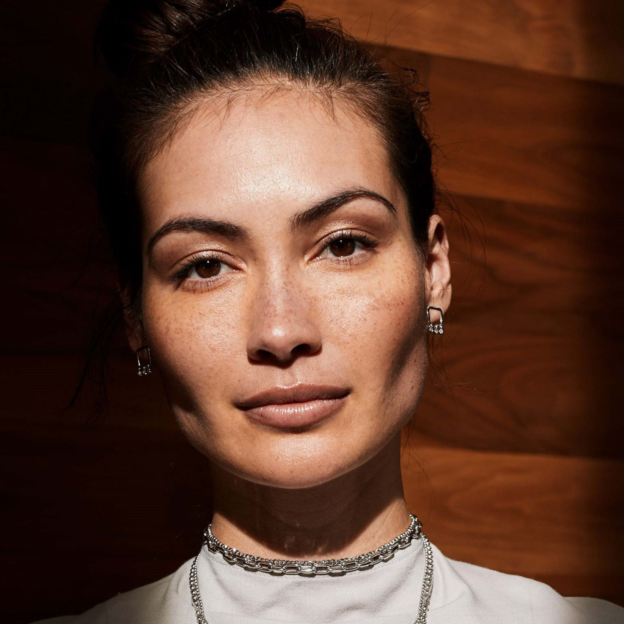 14k white gold open square post earring with bezel set diamond dangles shown on model with blurred wooid grain background