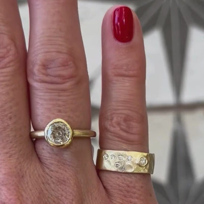 Candid video close up of hand wearing two rings, one is an old european-cut beel solitaire with hammered wide band and scattered diamond pinky ring. blurred background.