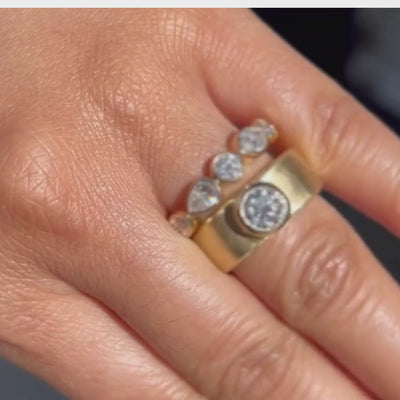 Candid video close up of hand wearing extra wide cigar band bezel diamond solitaire ring with marquise and round diamond eternity band.