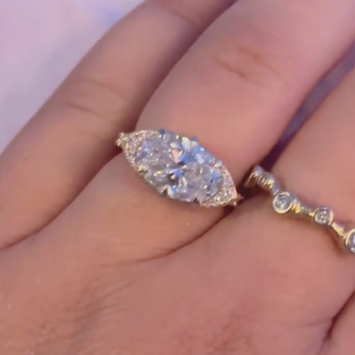 Candid close up video of hand wearing east west oval-cut center stone with cat eye half halo design.