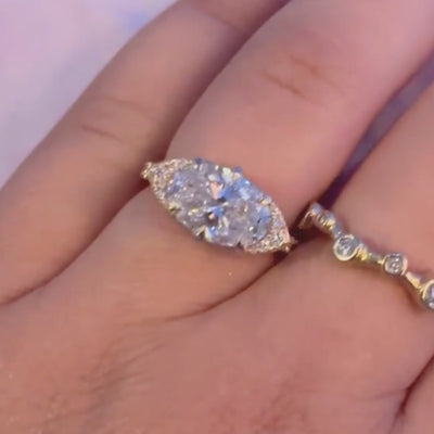 Candid close up video of hand wearing east west oval-cut center stone with cat eye half halo design.