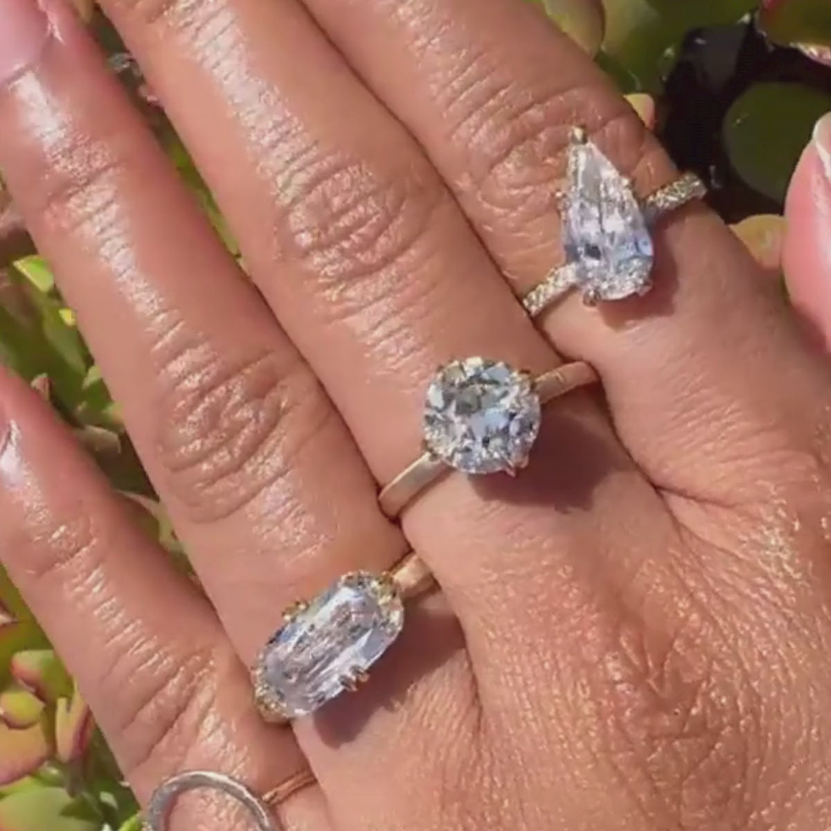 Close-up video of hand wearing diamond rings featuring tilted orientation pear-cut solitaire engagement ring with pave band.