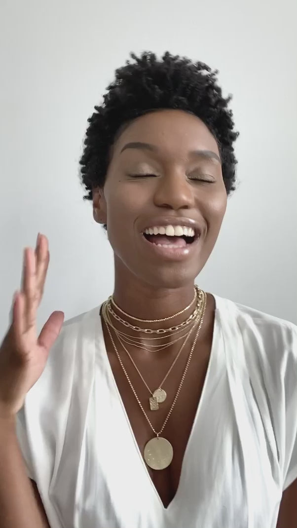 14k yellow gold necklace stack including the moca necklace stacked with the mica chain and the chai three strand diamond cut ball chain necklace stacked with the skye and deft pendants and an extra large round medallion with scattered white diamonds and hand etched starbursts on model in lifestyle video