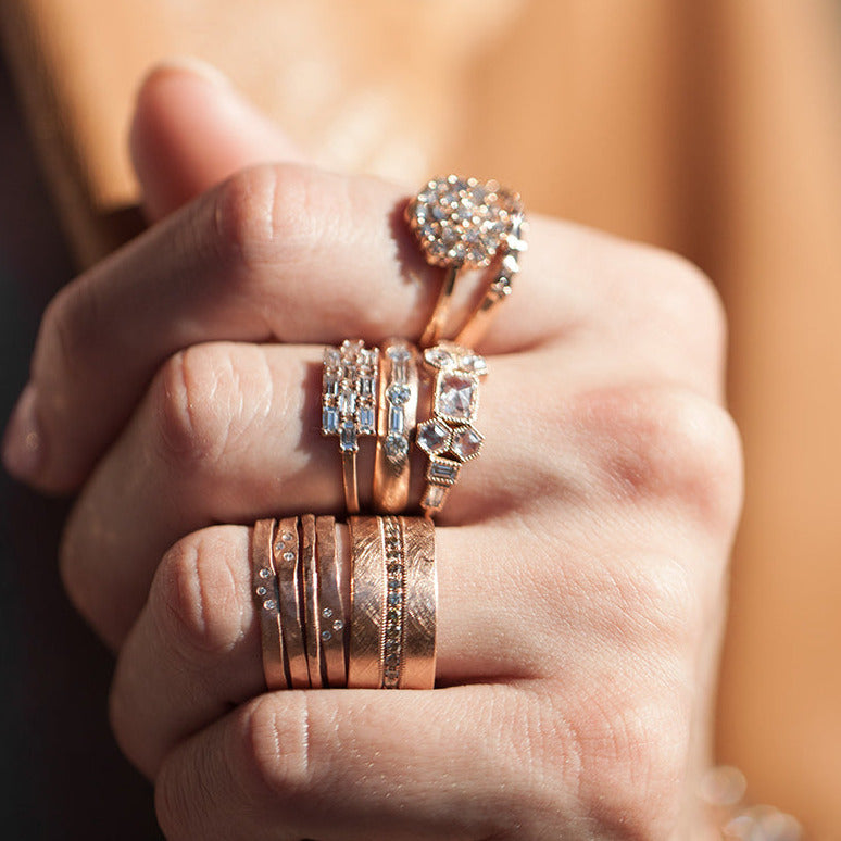 Hand wearing multiple rose gold rings with diamond accents against a blurred background