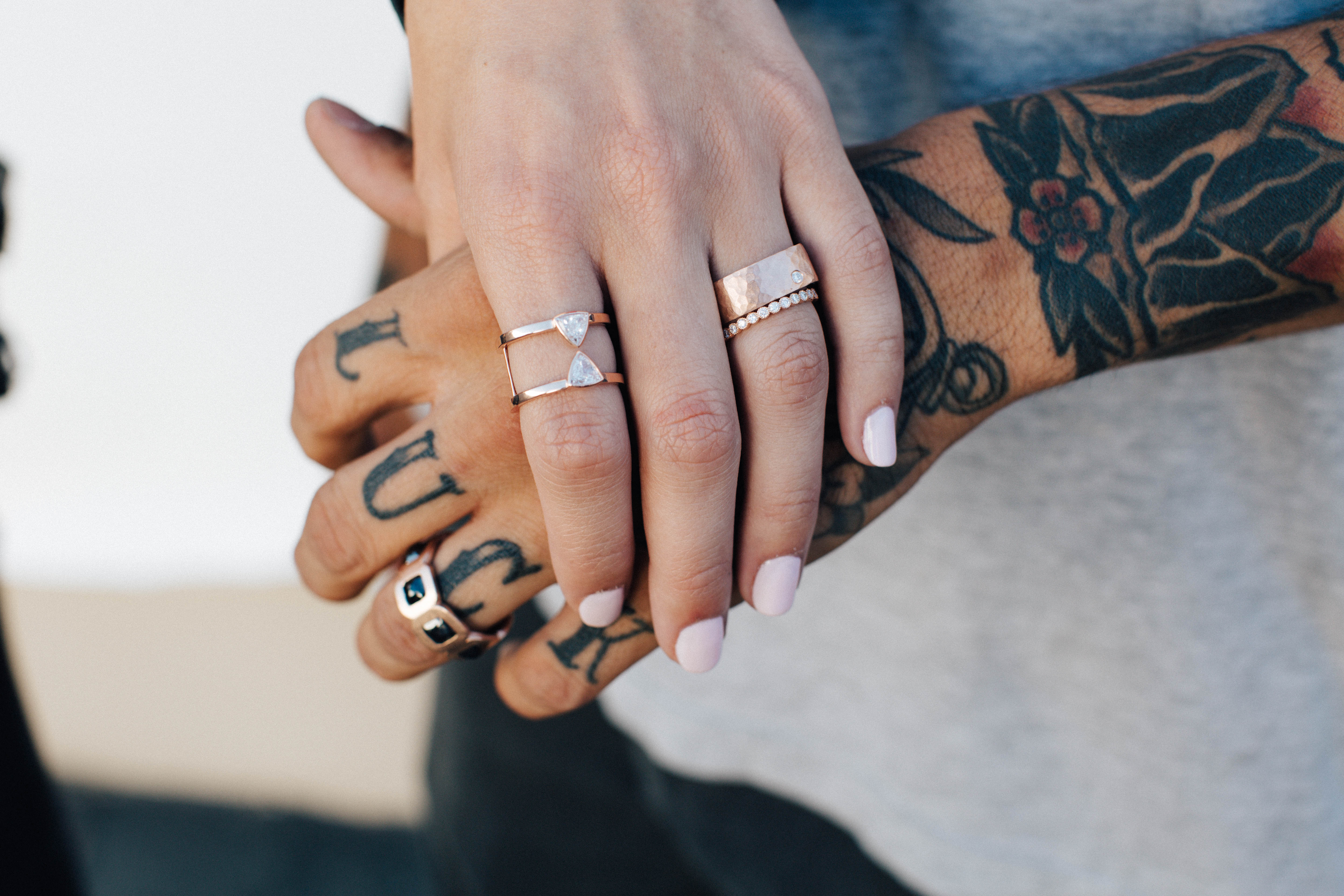 Close-up of hands with tattoos and rings featuring stacked rose gold diamond thick, thin and statement bands lifestyle shot with a blurred background