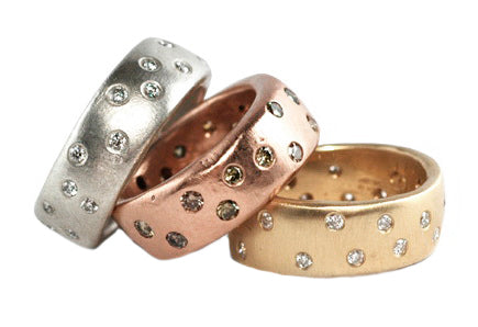 Three colored gold rings with scattered white diamonds embedded in a wide band on a white background