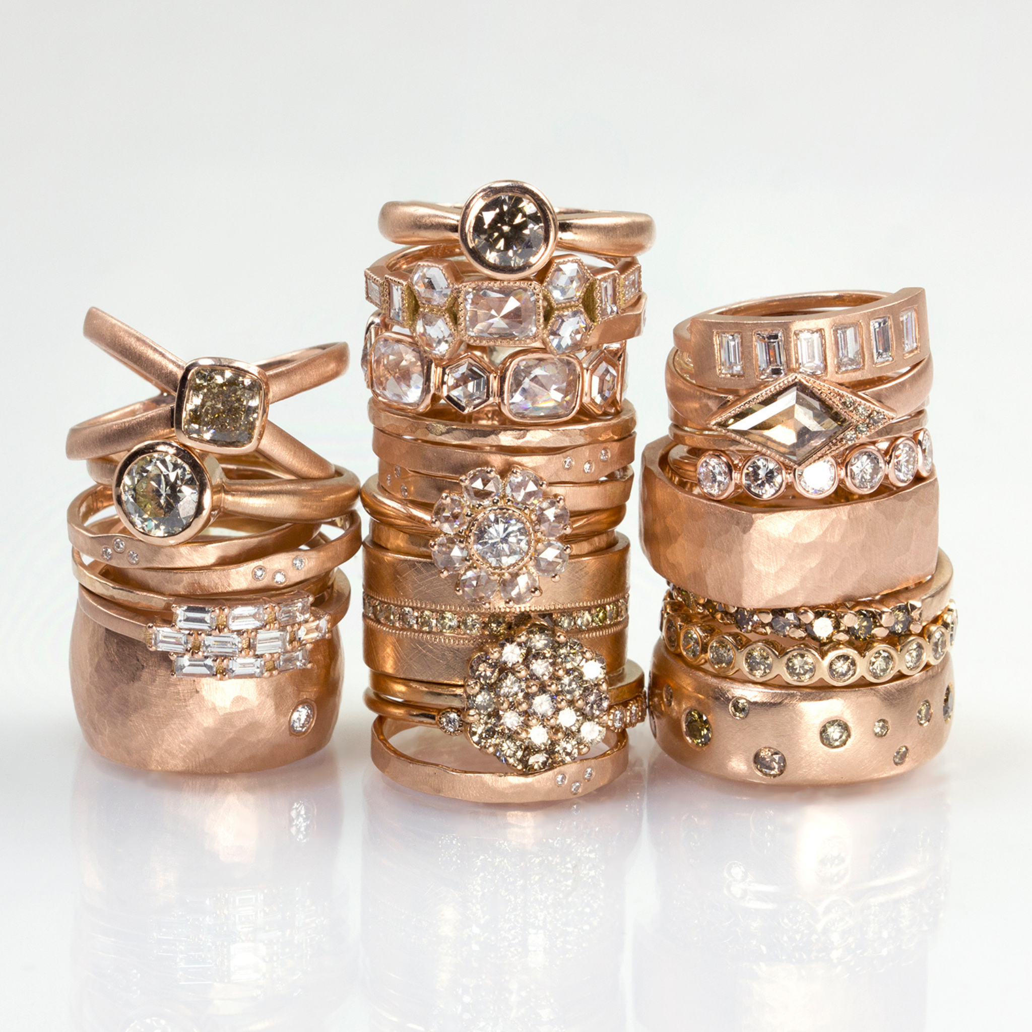 Stacks of rose gold engagement rings and wedding bands with white and cognac diamonds, unique designs and stone shapes on a white background