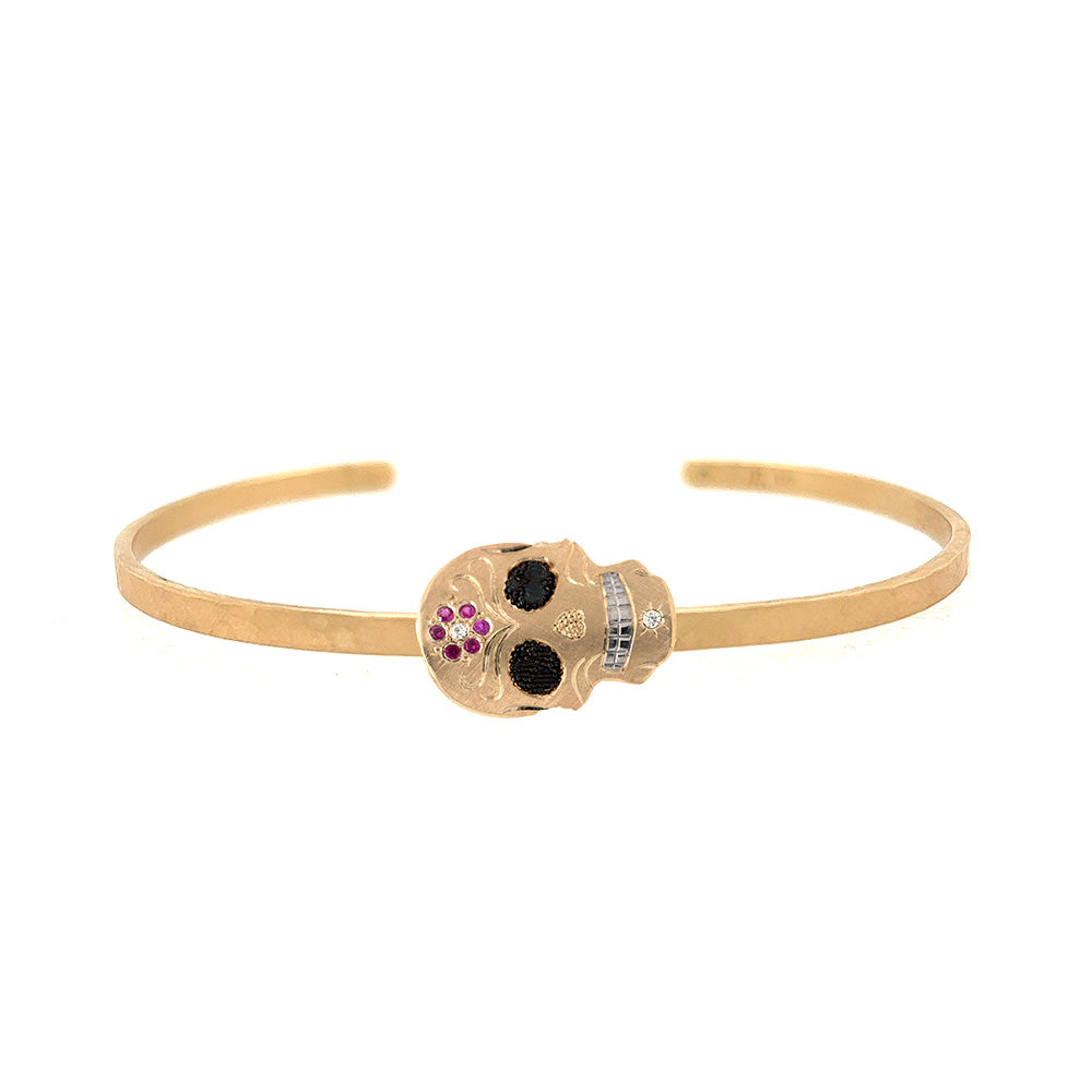 14k yellow gold skull-shaped cuff bracelet with gemstones and rhodium brightened teeth on a white background