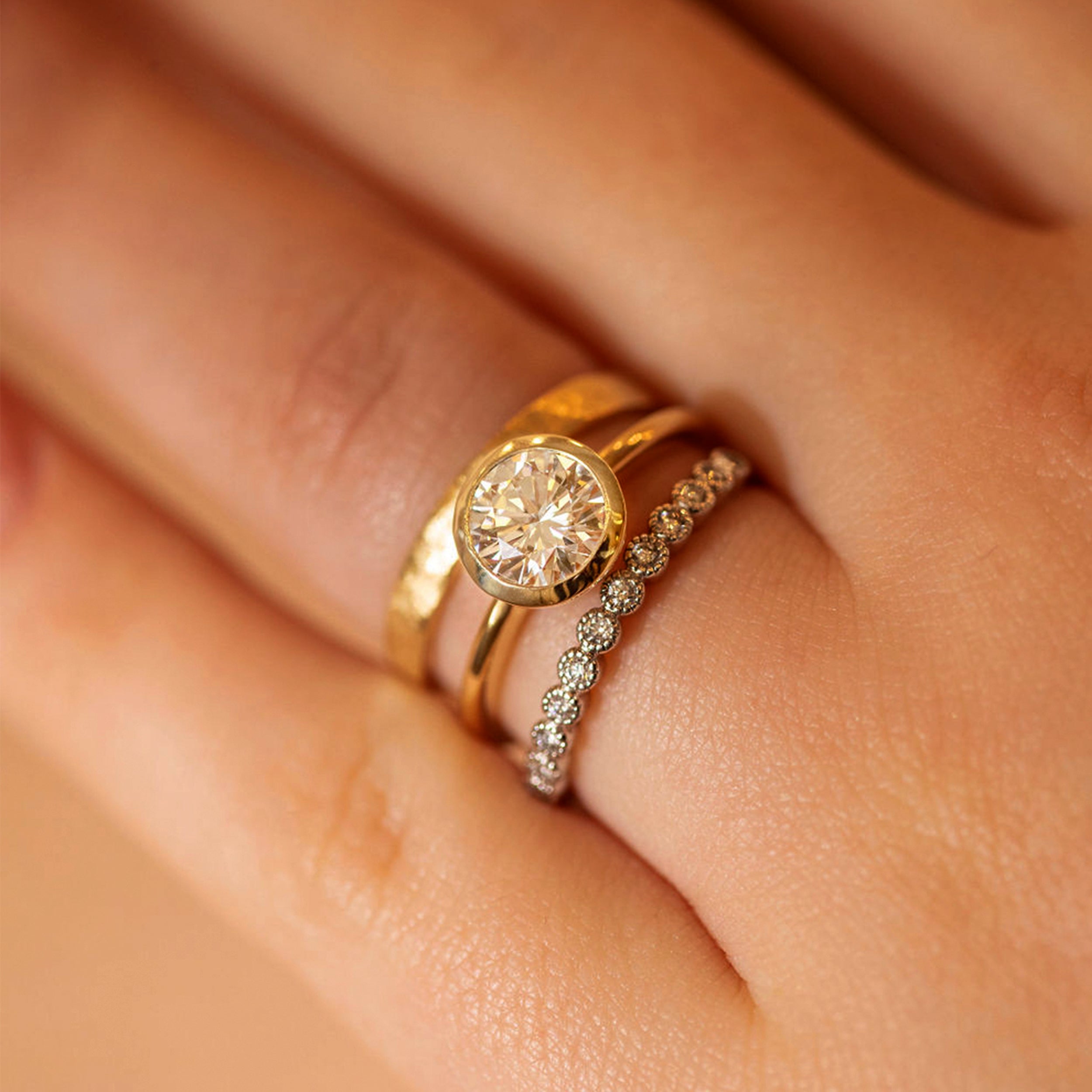 Close-up of a hand wearing two gold rings with diamond accents on a soft skin background