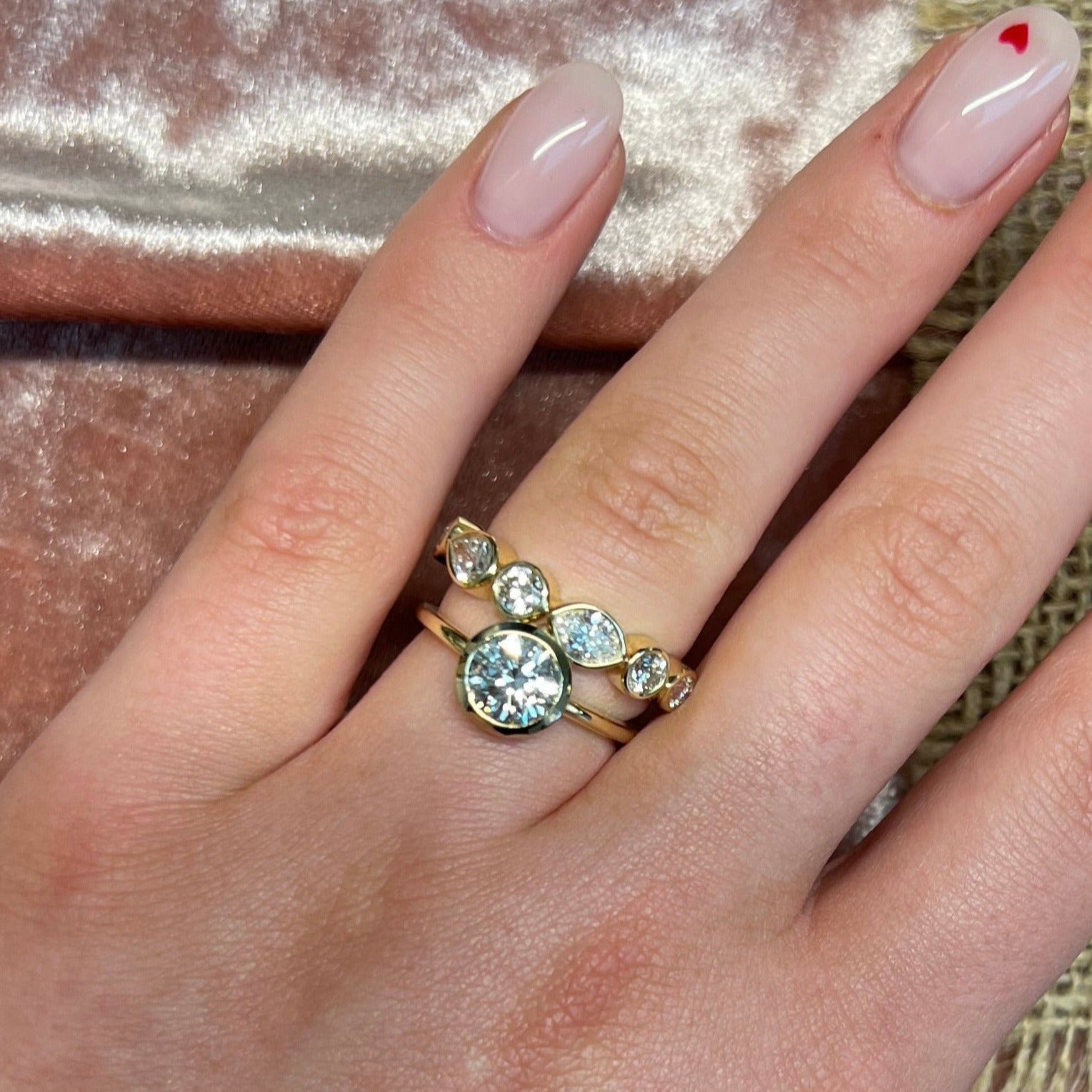 Hand wearing a gold ring with a large bezel set  gemstone and large marquise eternity band on a textured fabric background