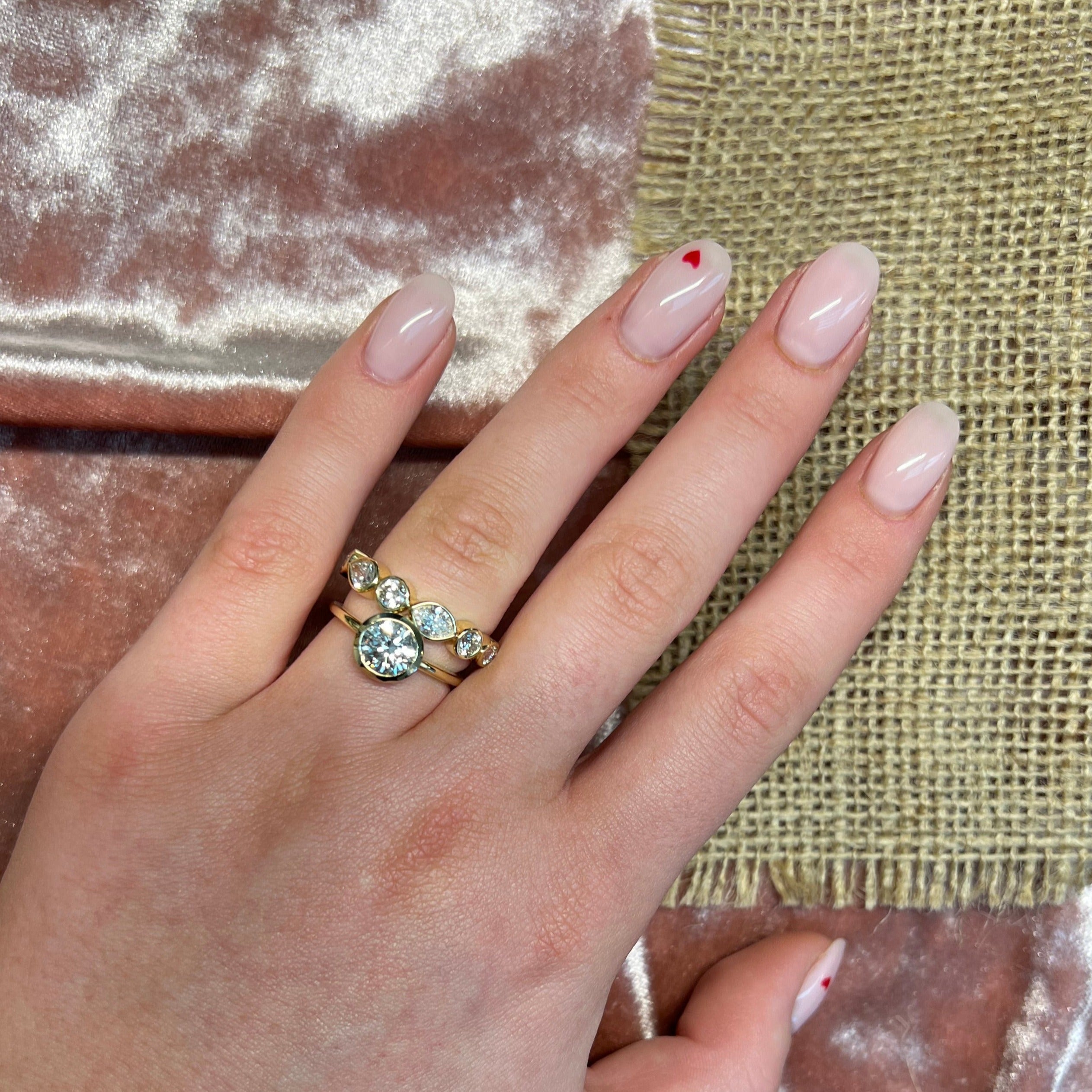 Hand wearing a gold ring with a large bezel set  gemstone and large marquise eternity band on a textured fabric background