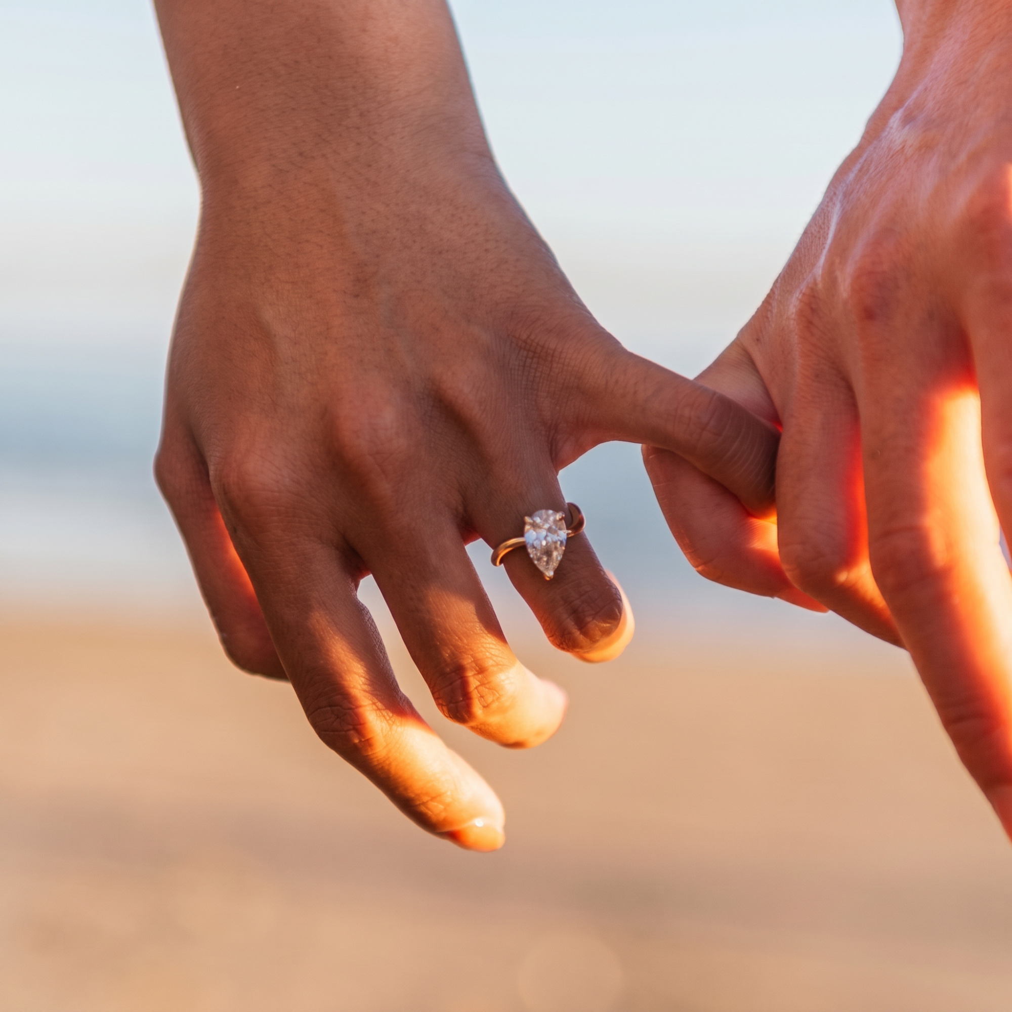 Solitaire pear cut diamond engagement ring with prong set asymmetric band in 14k yellow gold, second lifestyle shot on a model's hands