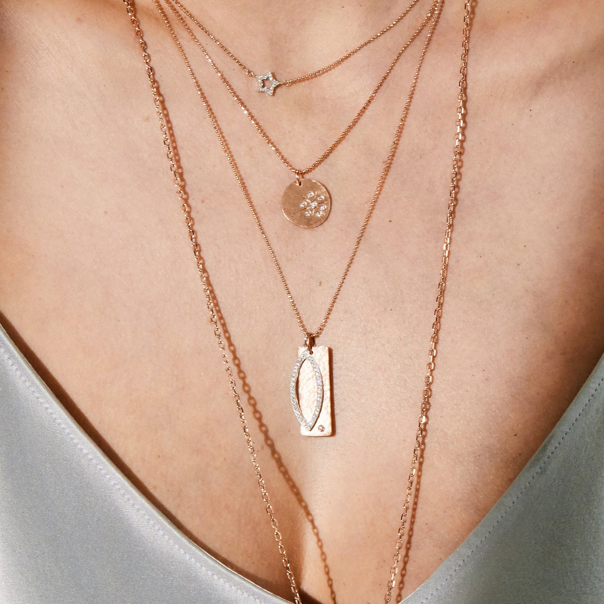 Woman in gray satin dress wearing layered gold necklaces and earrings against a red background