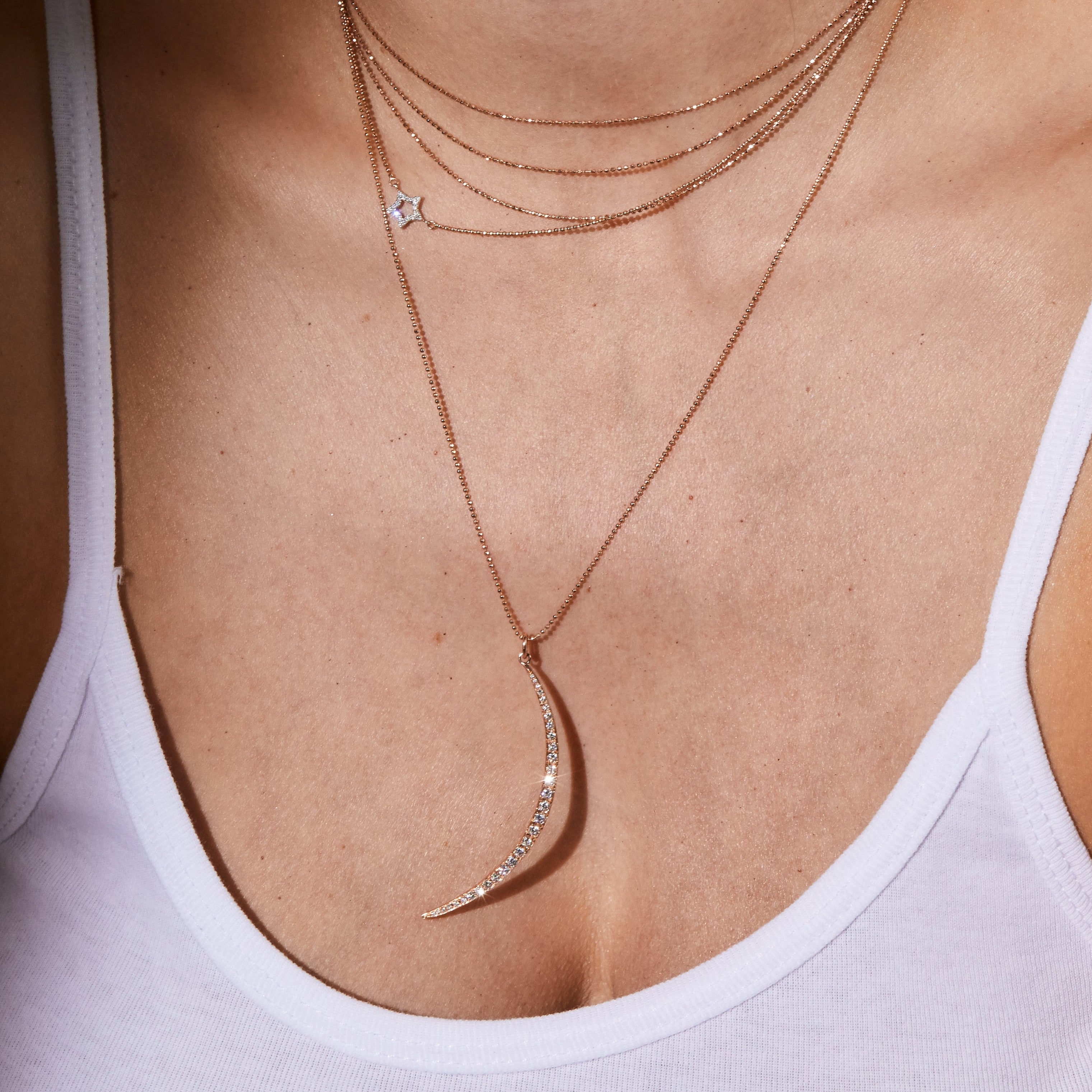 Close-up of a person wearing yellow gold star and moon pave diamond pendants on dainty diamond ball chain necklaces and earrings 