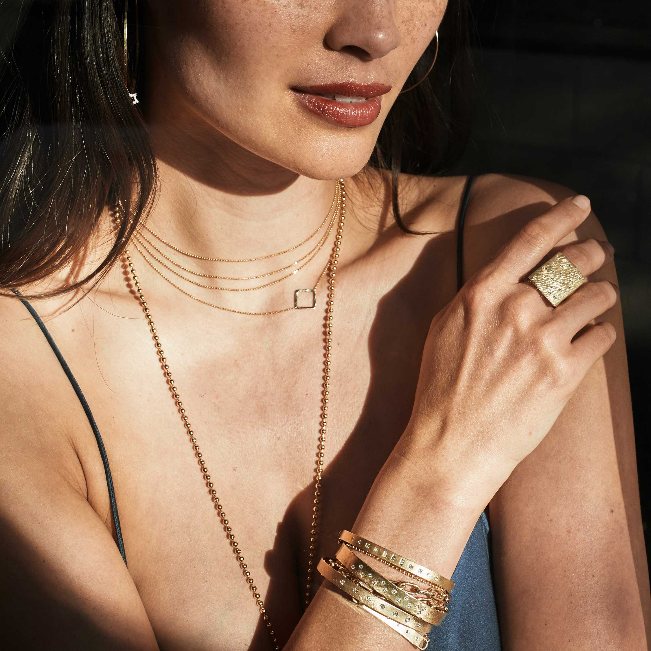 Beautiful model wearing layered 14k yellow gold jewelry. 14k gold CHAI 4 strand dainty necklace, lare rectangular ring and several bracelets accented with diamonds.