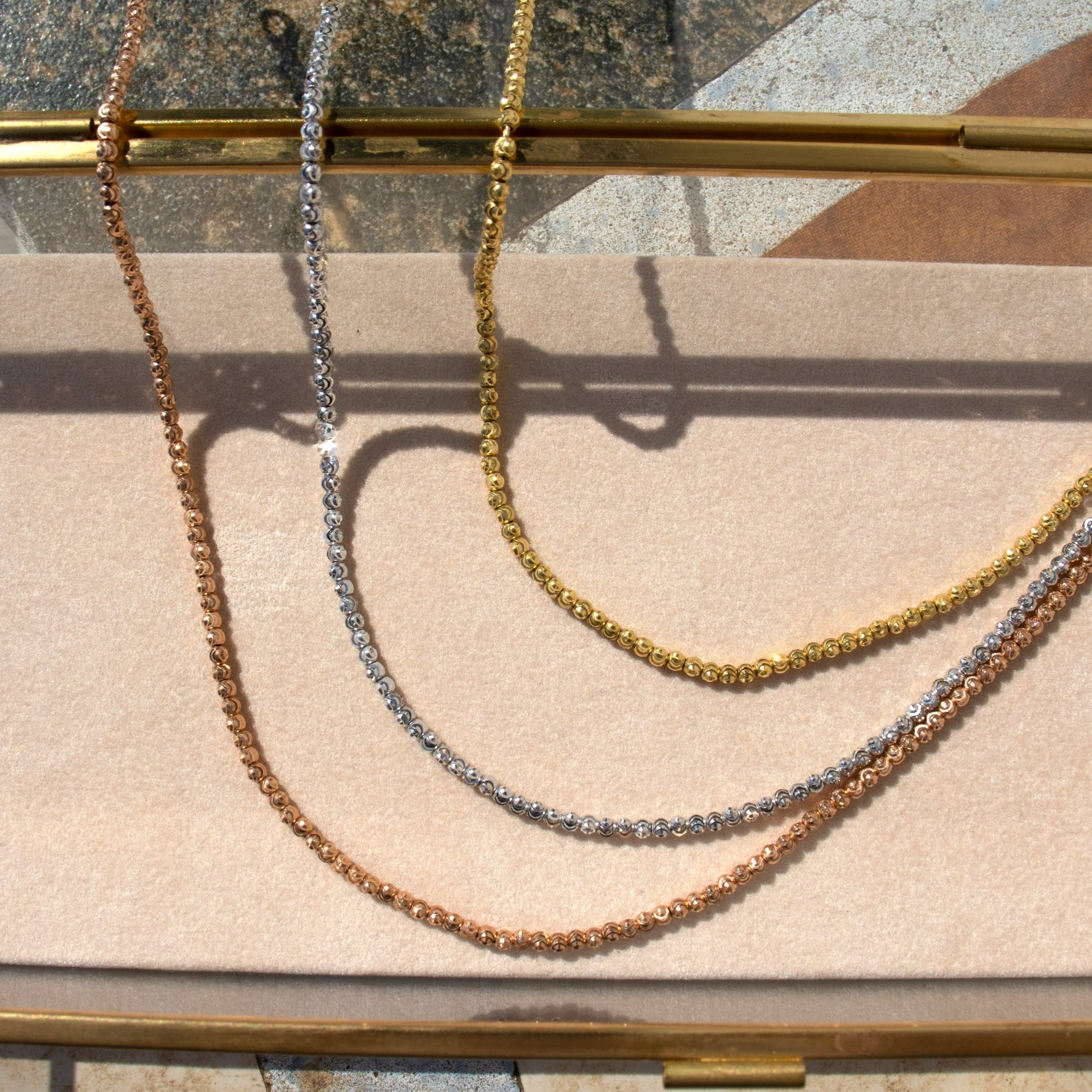 14k gold mooncut faceted bead necklaces in yellow, rose, white gold shown in display.