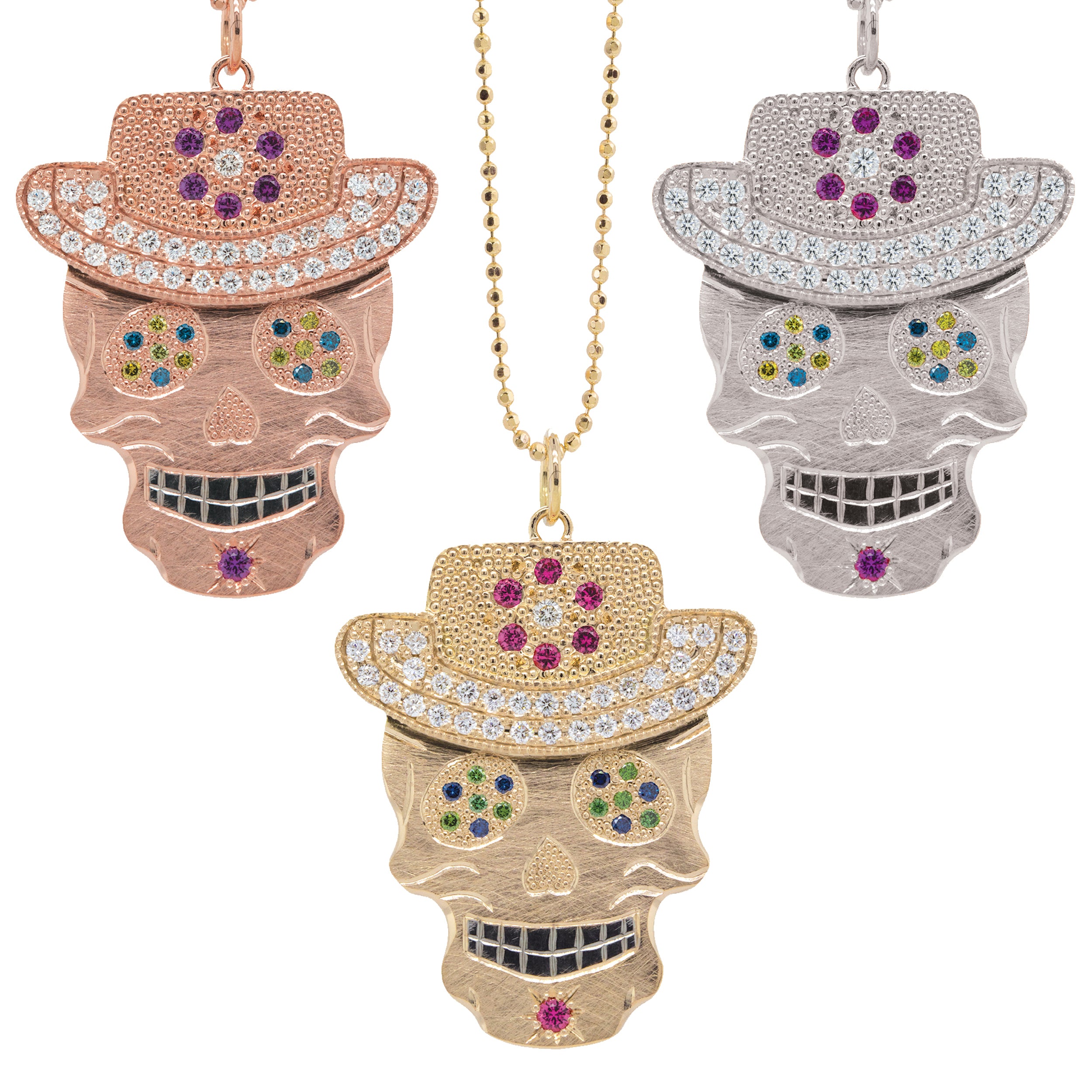 Grouping of 3 varieties of vibrant our original Ghostrider Collection Vaquero gemstone encrusted sugar skull XL pendants. Candy skull wearing cowboy hat  rhodium darkened teeth. Shown in 14k rose,yellow and white gold mixed diamond sapphires and Tzavorite. Fine detail engraving, milgrain details. Pink sapphire floral detail and diamond encrusted brim on hat. Eyes with green Tzavorite and blue sapphire pave set gemstone eyes.  Shown on 2.0mm ball chain.