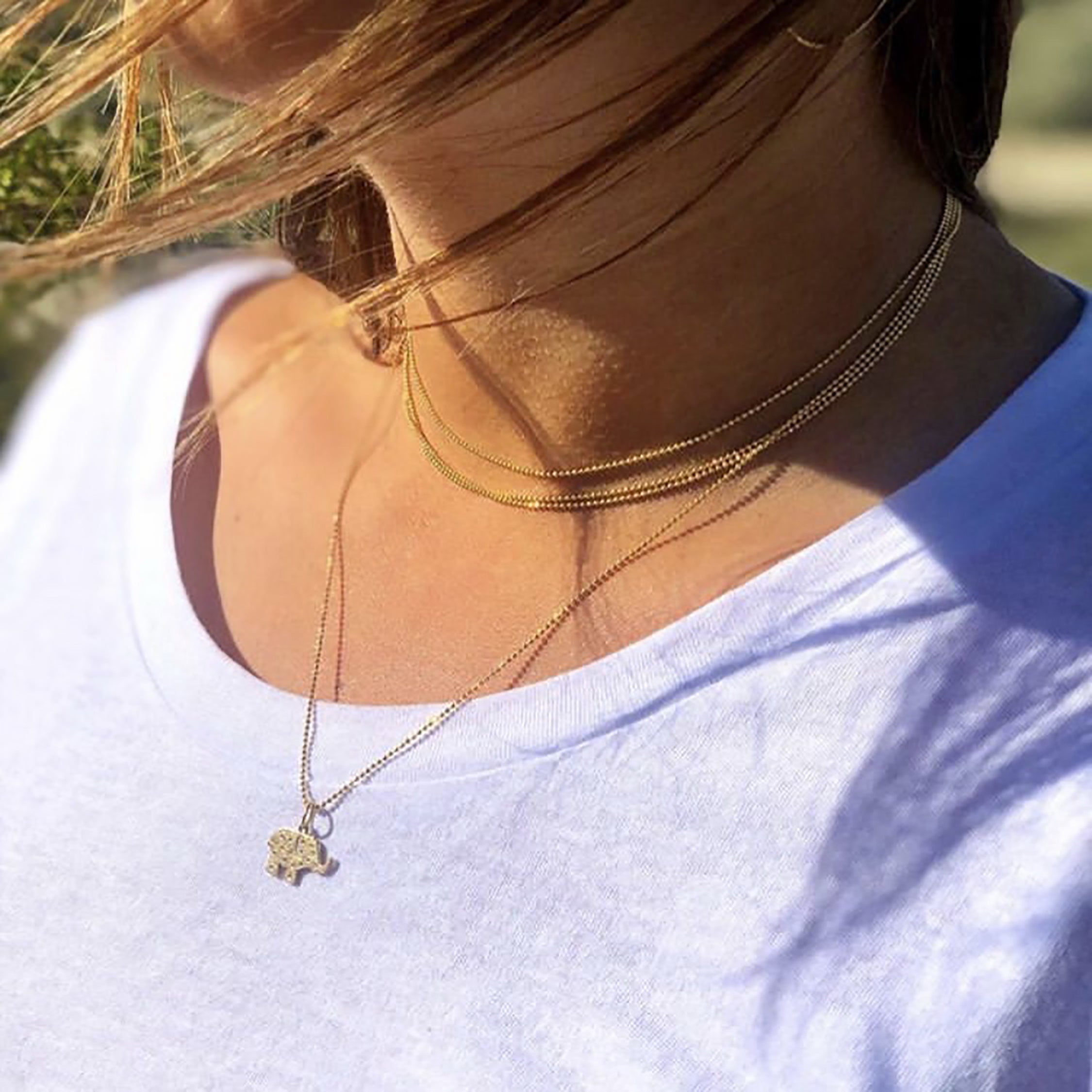 14k yellow gold baby ELLI elephant charm with scattered diamonds and sapphire eye on model