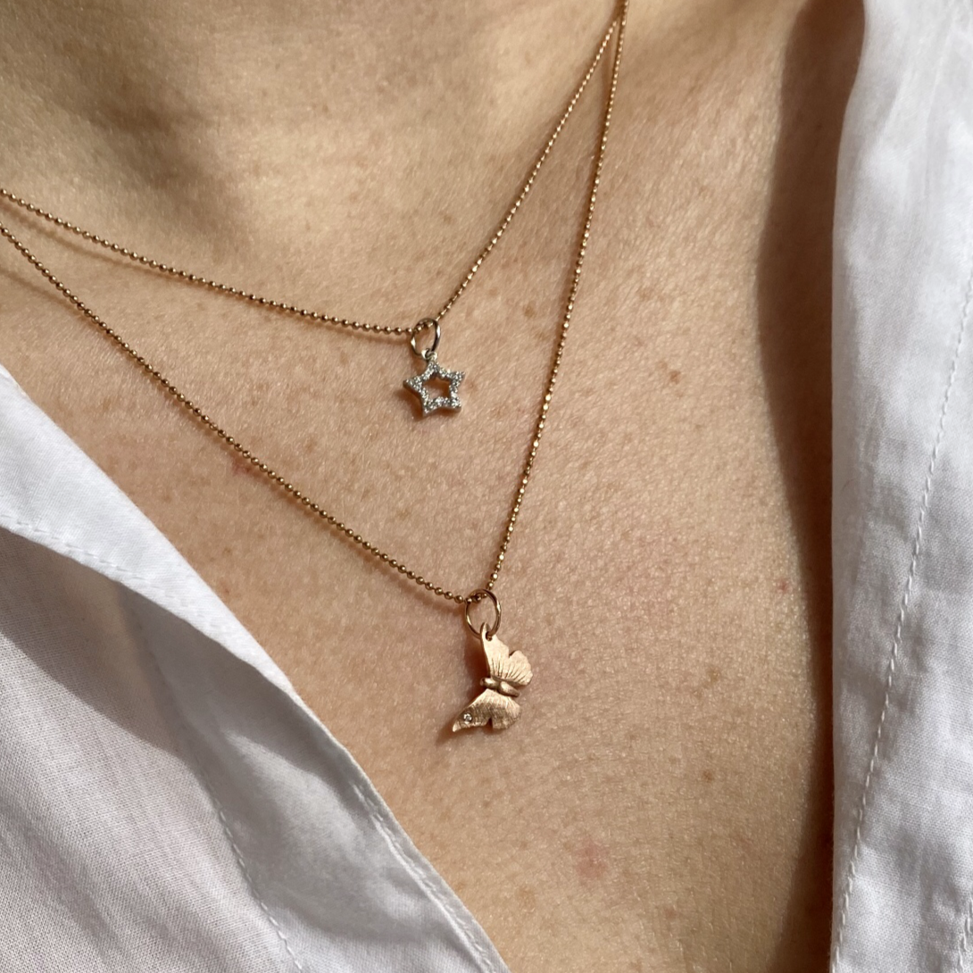 14k gold baby ANNA butterfly charm with one diamond on model with STAR pendant